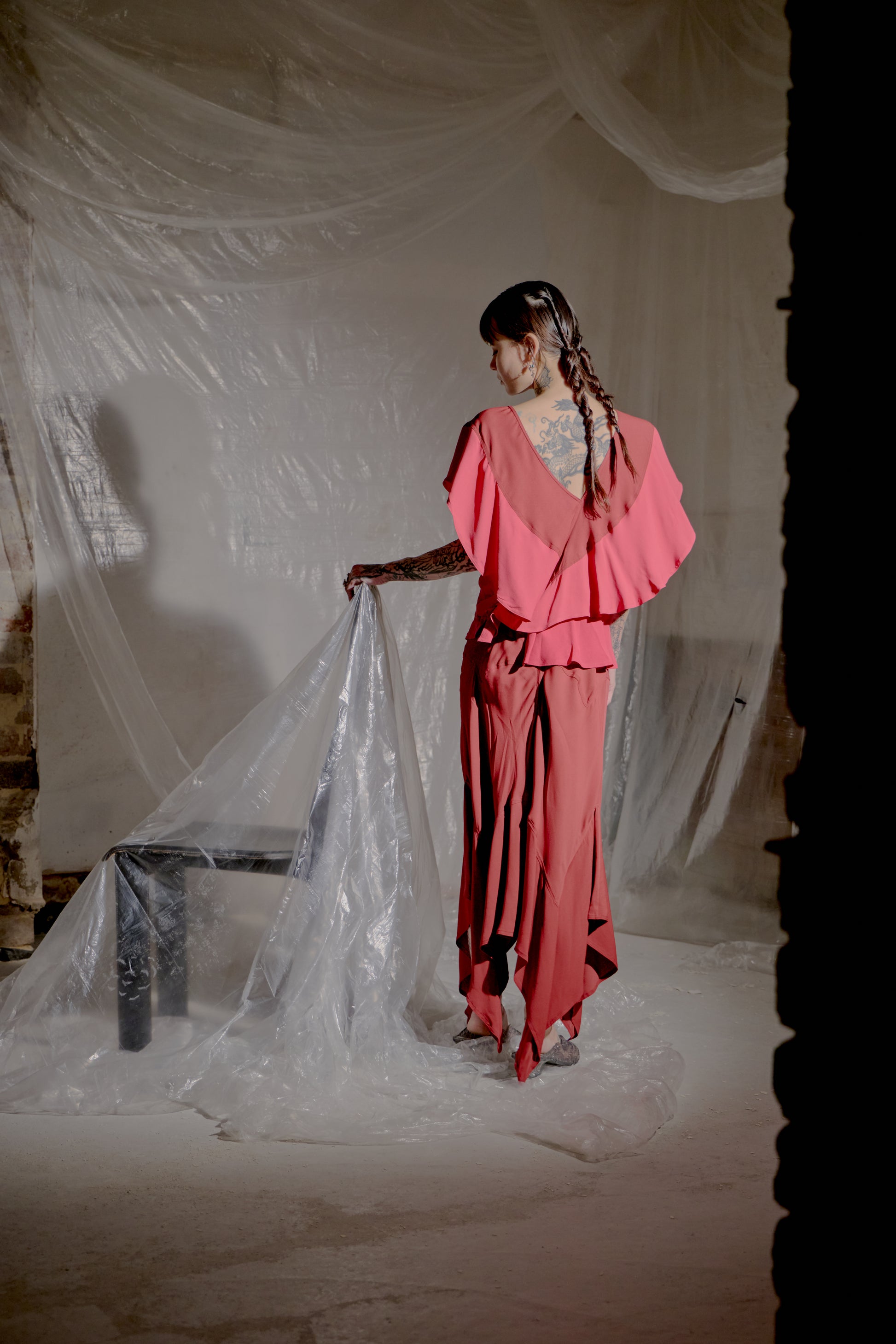 Person in a pink Saint Laurent outfit holding a transparent sheet in a dimly lit room.