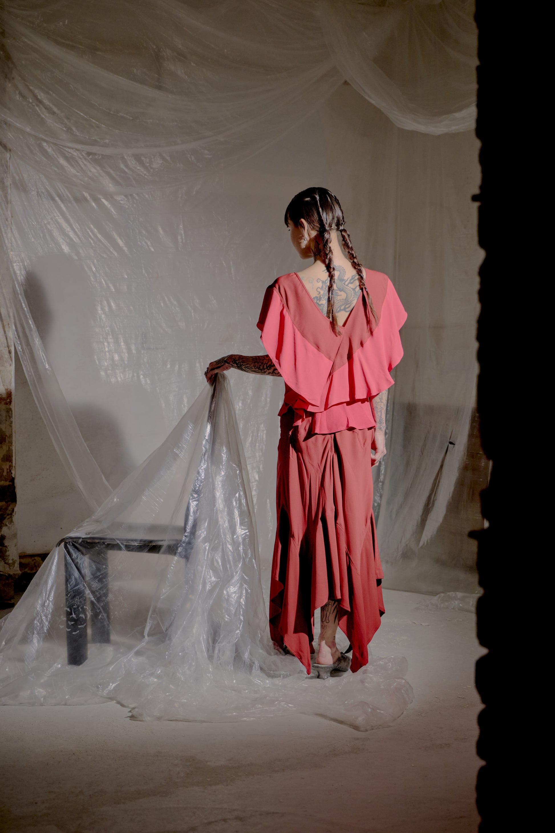 Person in a pink Saint Laurent outfit standing in a softly lit room with draped fabric.