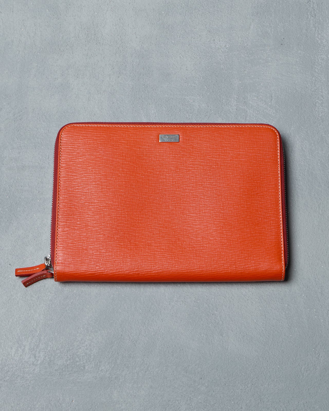 Orange leather Salvatore Ferragamo pouch with a zipper on a gray background