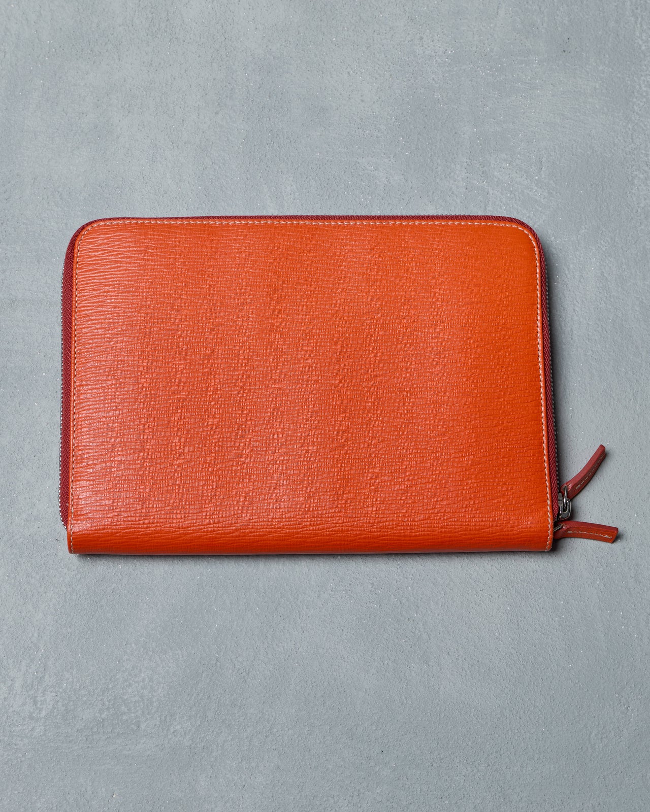 Orange leather Salvatore Ferragamo pouch with a zipper on a gray background