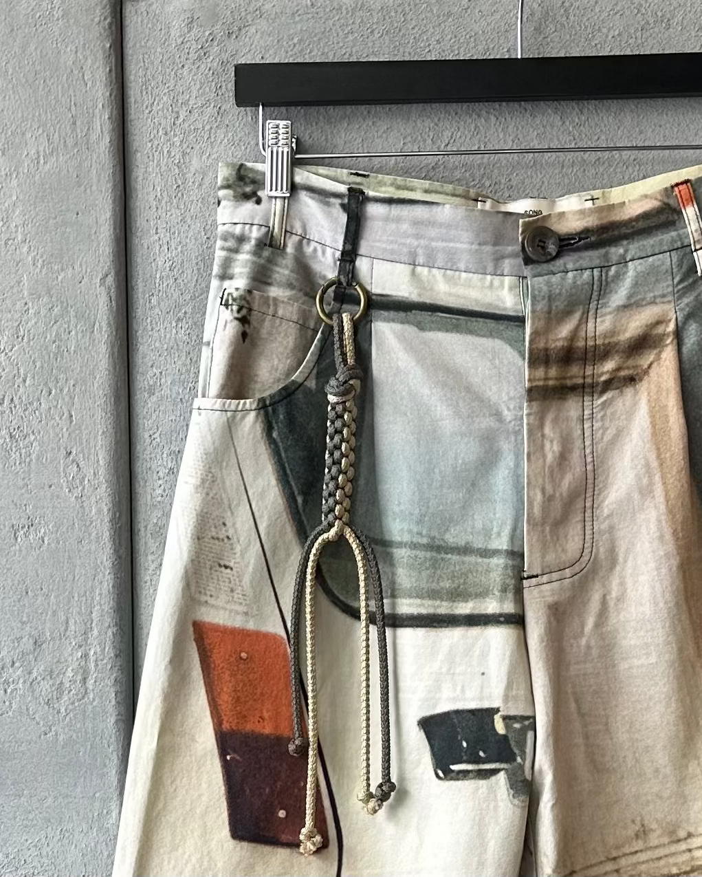 Song For The Mute Pants with abstract design hanging on a gray wall