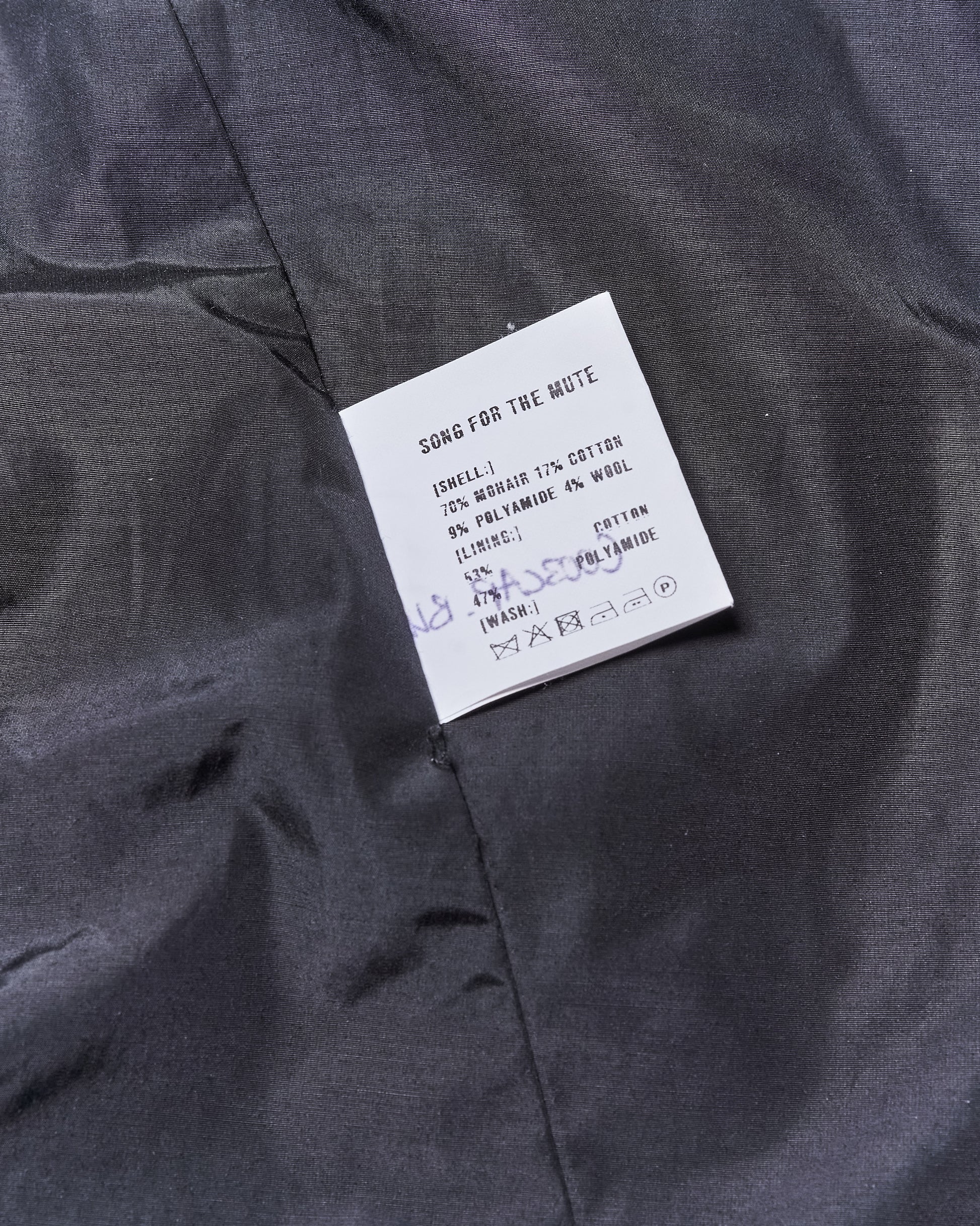 Clothing label on dark Song For The Mute jacket fabric, detailing material composition: 70% mohair, 17% cotton, 9% polyamide, 4% wool. Includes wash symbols.