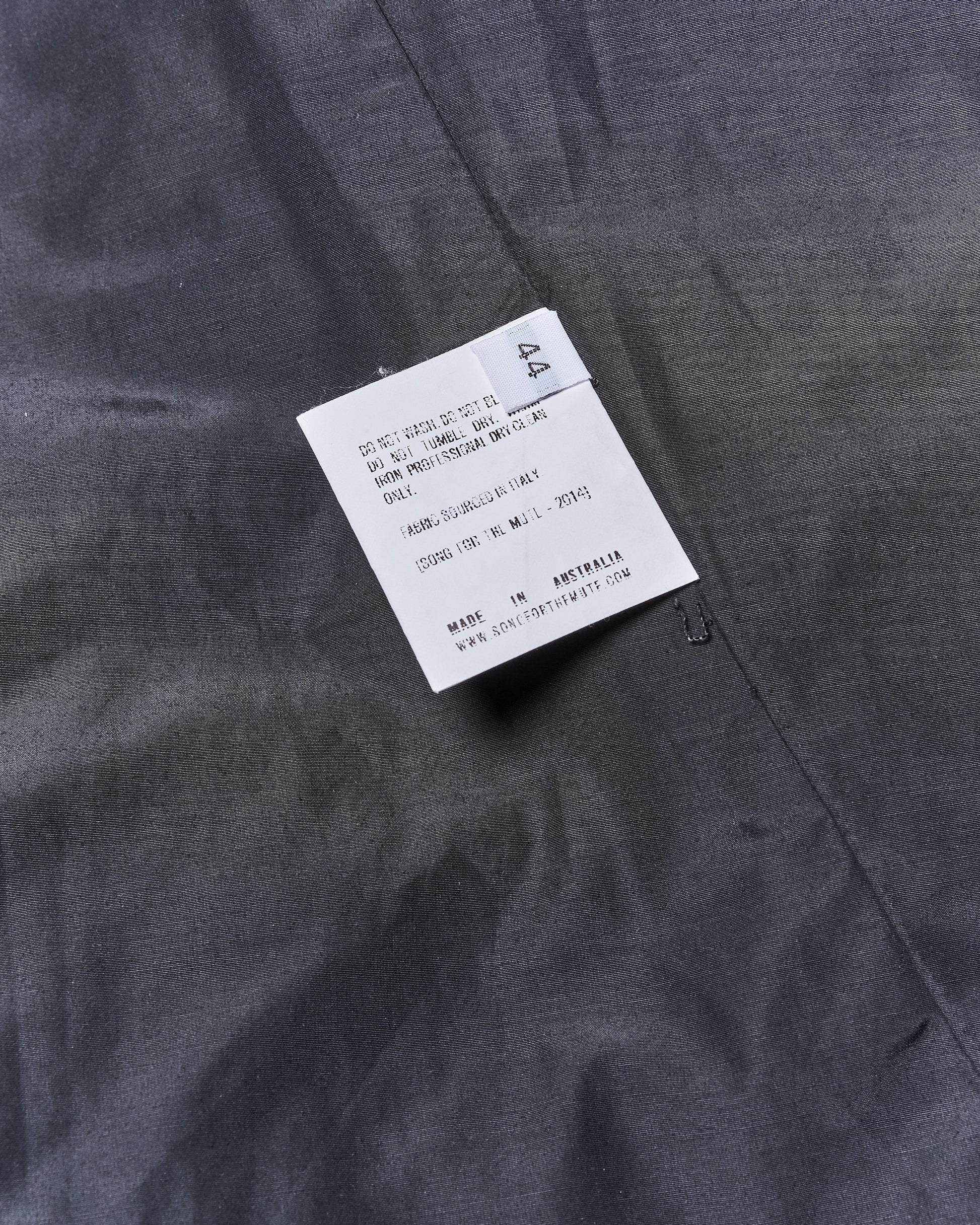 White clothing label on gray Song For The Mute jacket fabric with washing instructions in English. Notable keywords include "Made in Australia." Fabric appears textured.