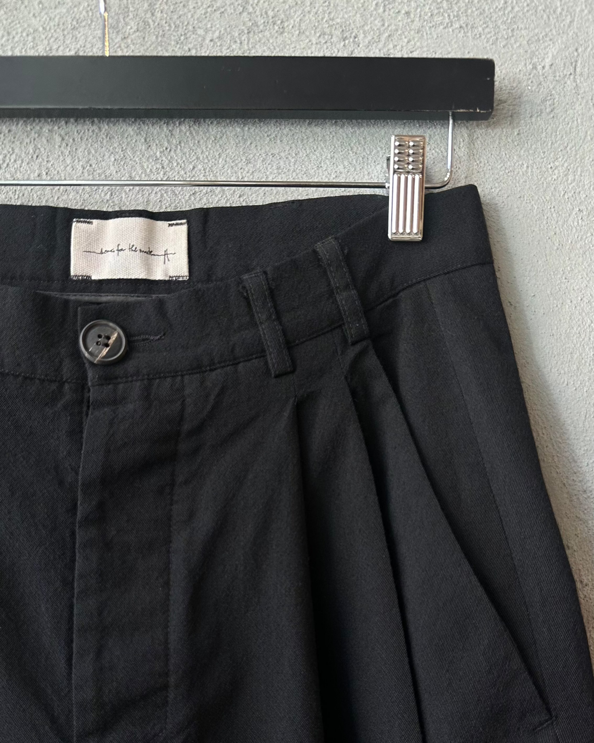 Black Song For The Mute pants hanging on a hanger against a gray wall