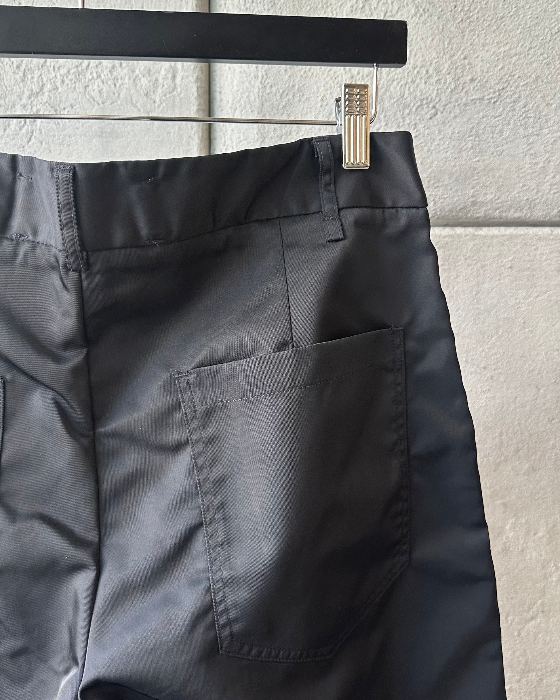 Close up of black Song For The Mute pants hanging on a rack against a light gray wall.