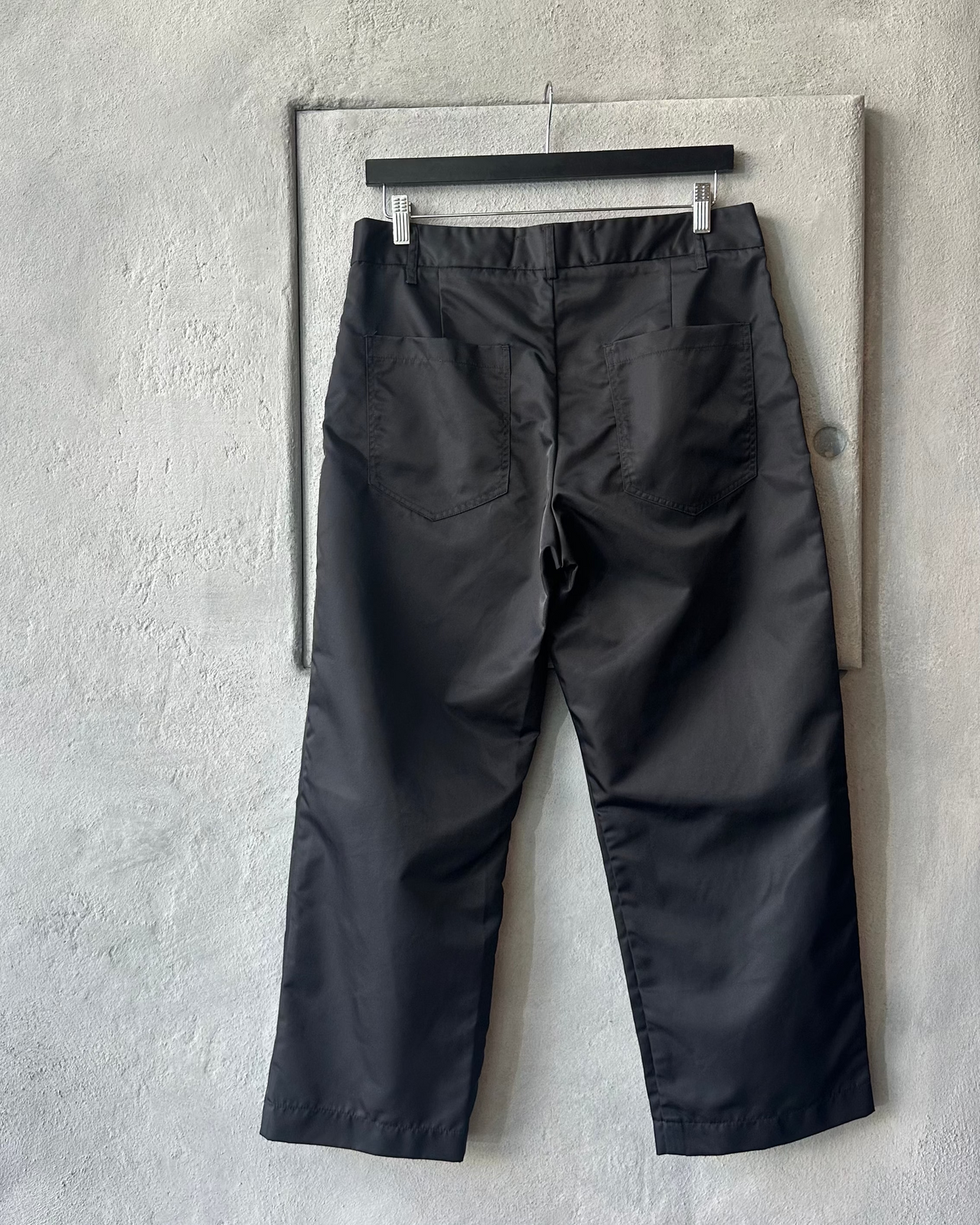 Black Song For The Mute pants with a tag on a gray concrete wall