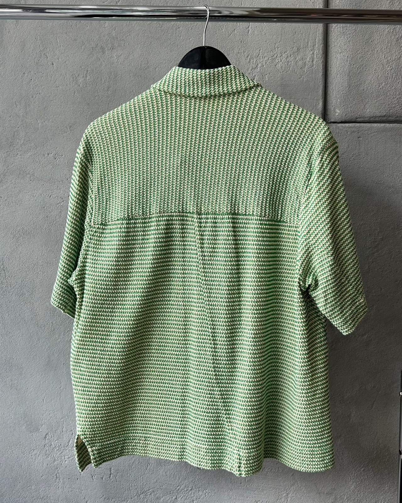 Green checkered Song For The Mute shirt on a hanger against a gray wall