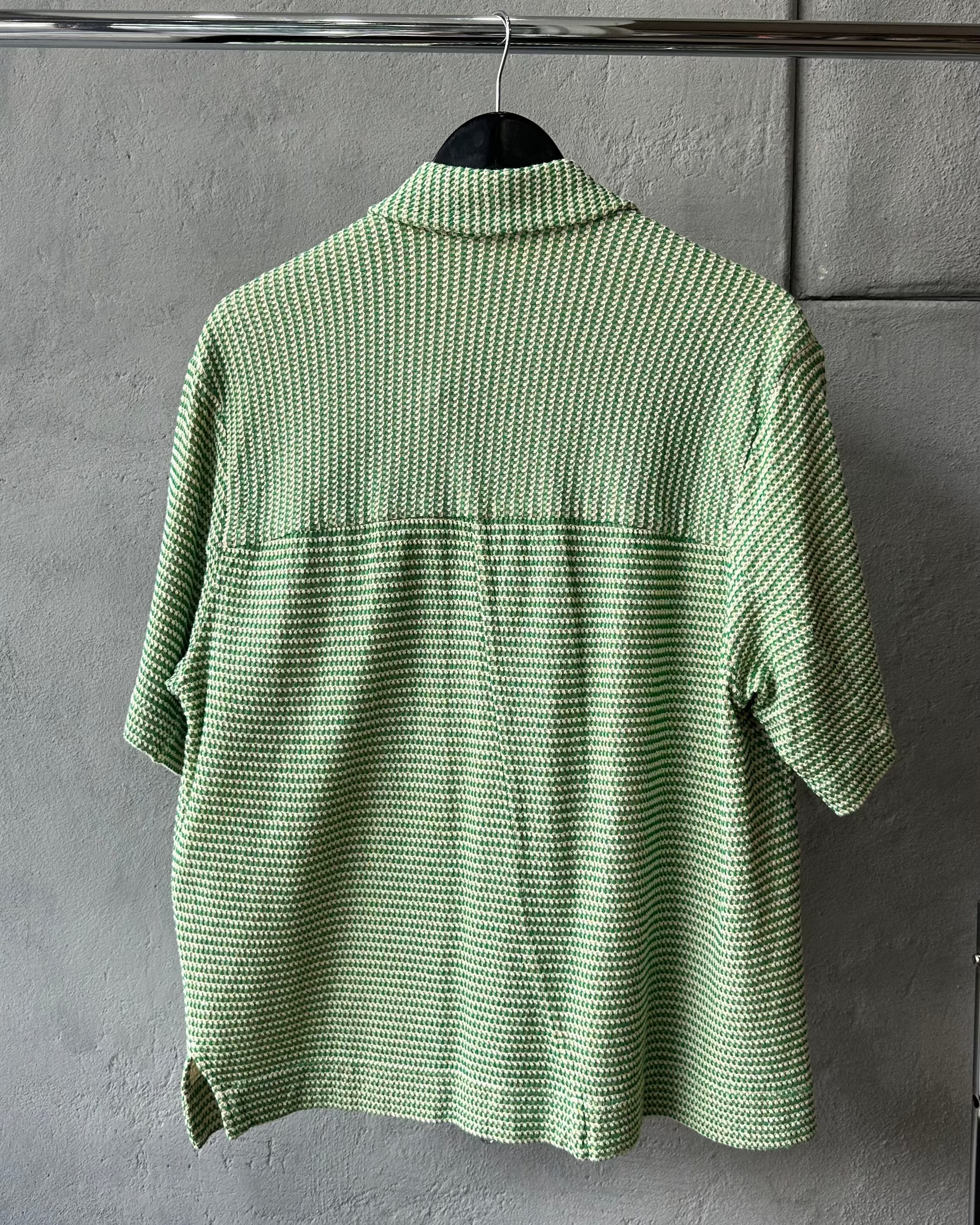Green textured Song For The Mute shirt on a hanger against a gray wall