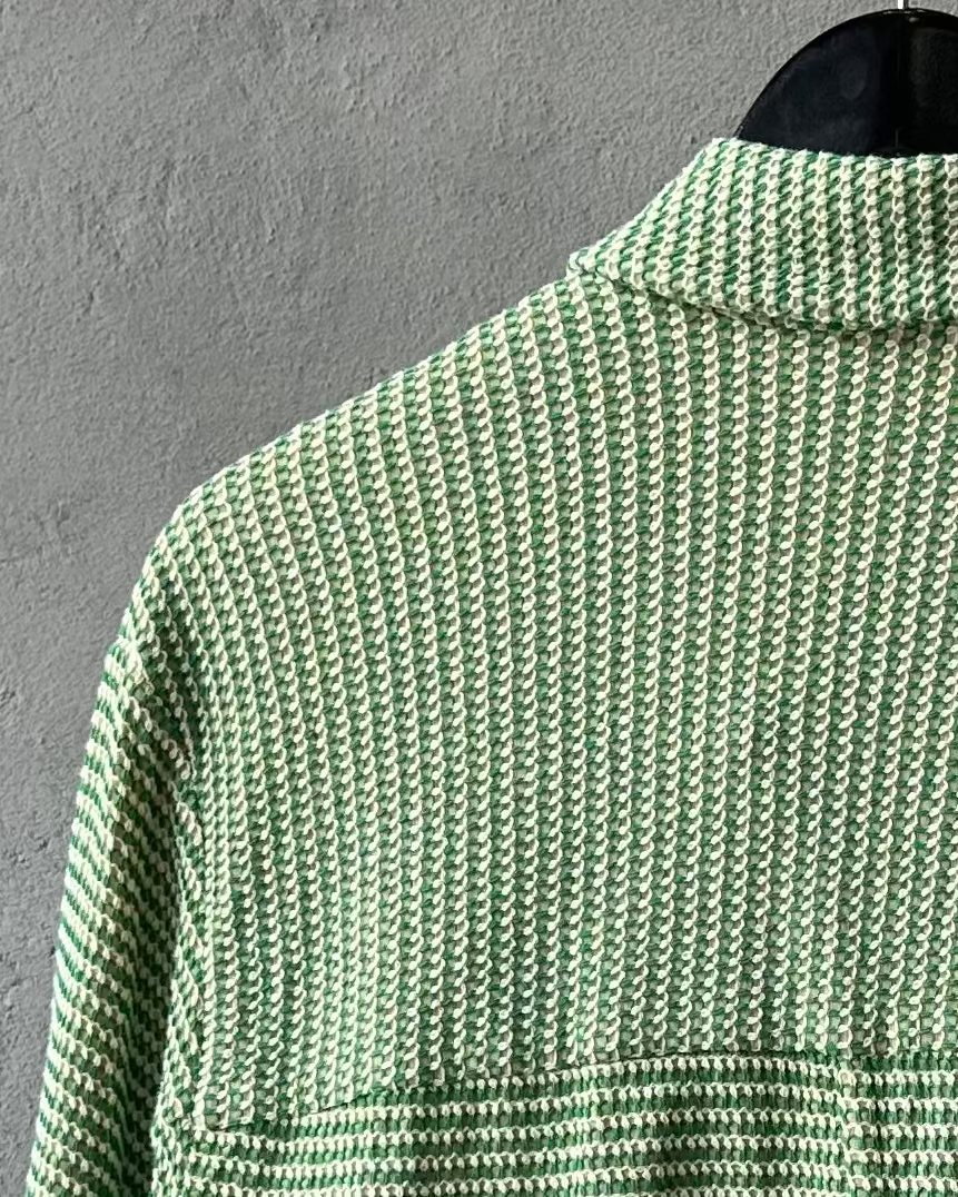 Green and white patterned Song For The Mute shirt on a hanger against a gray wall