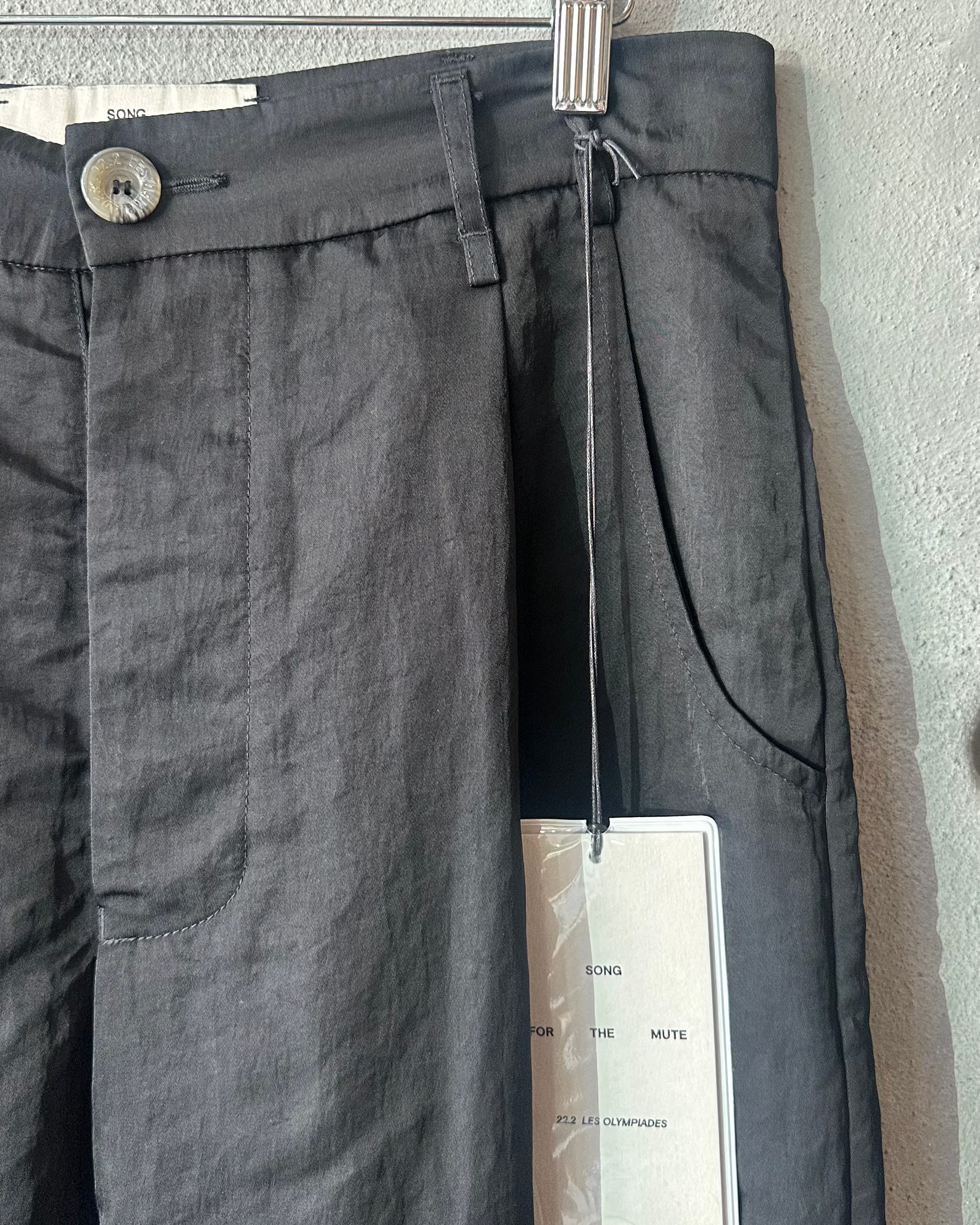 Black Song For The Mute pants hanging on a rack with a tag attached, against a gray wall.