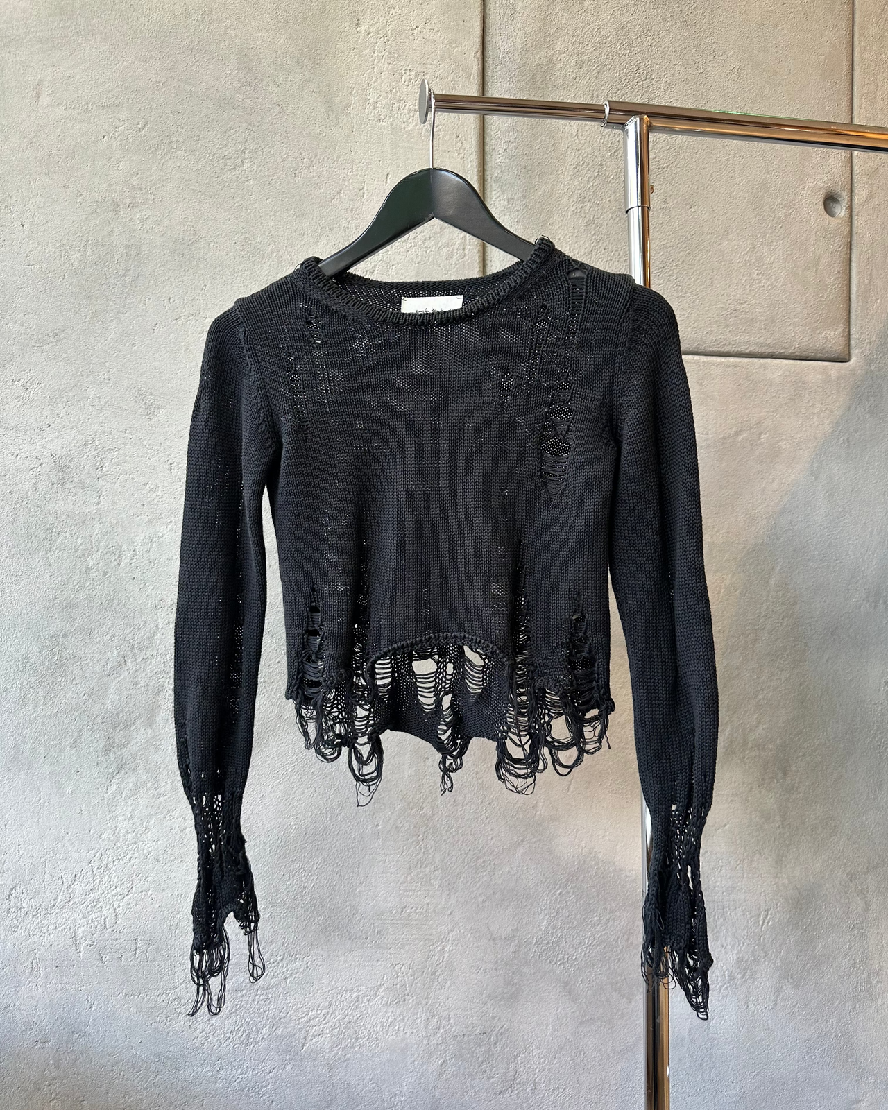 Black distressed Song For The Mute sweater on a hanger against a gray wall