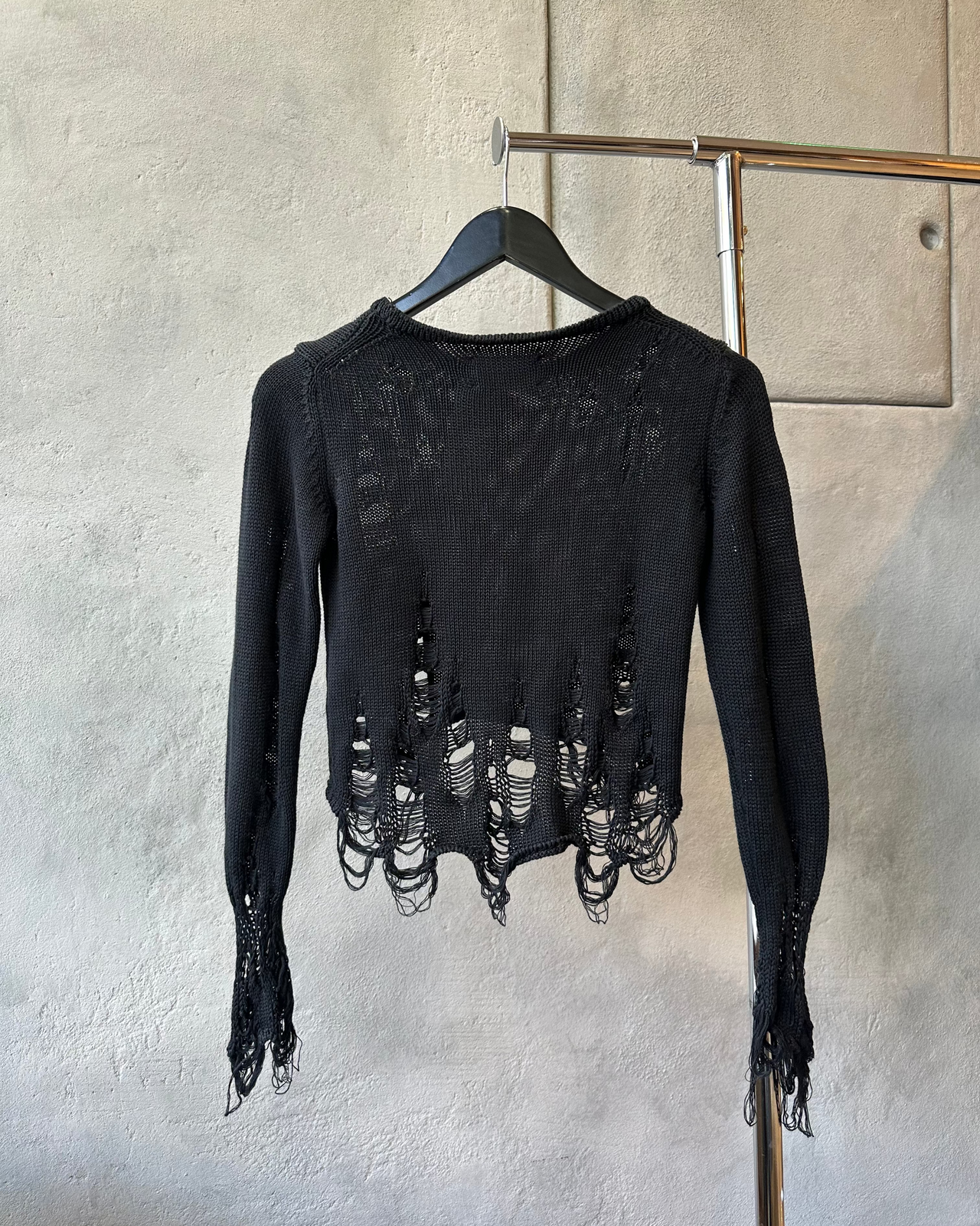 Black distressed Song For The Mute sweater on a hanger against a gray wall