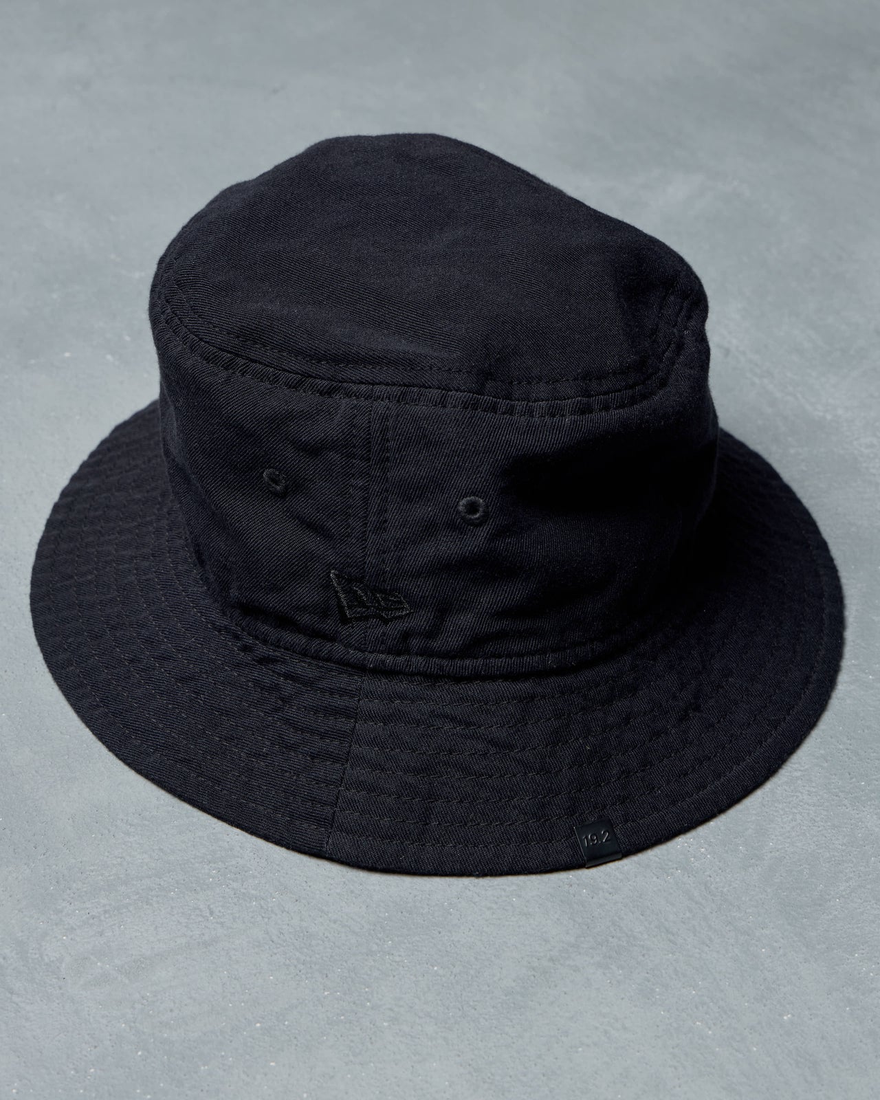 A black Song For The Mute x New Era bucket hat with subtle embroidered details sits on a light gray surface. 