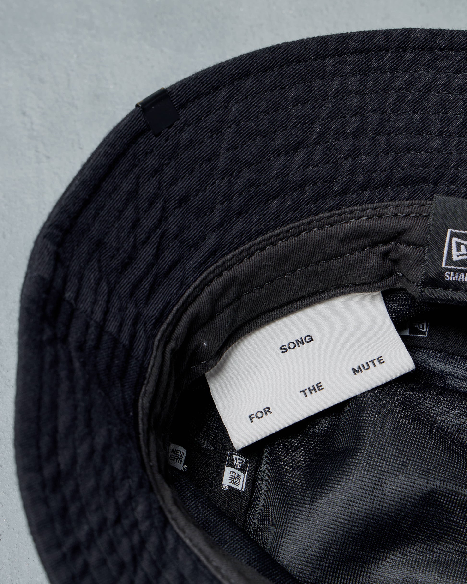 Black Song For The Mute x New Era bucket hat with a label inside on a gray background