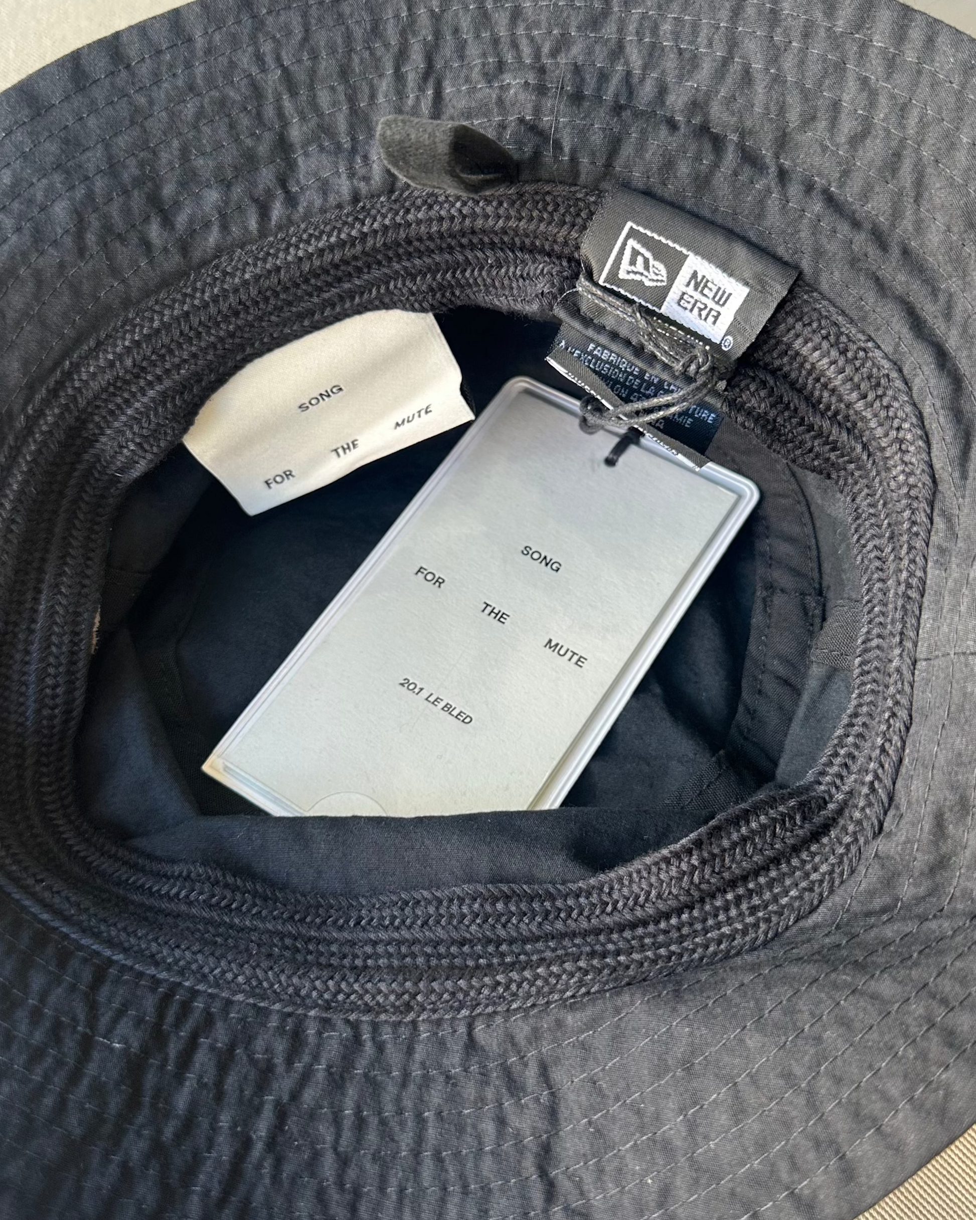 Black Song For The Mute x New Era bucket hat with tags inside, on a light gray background