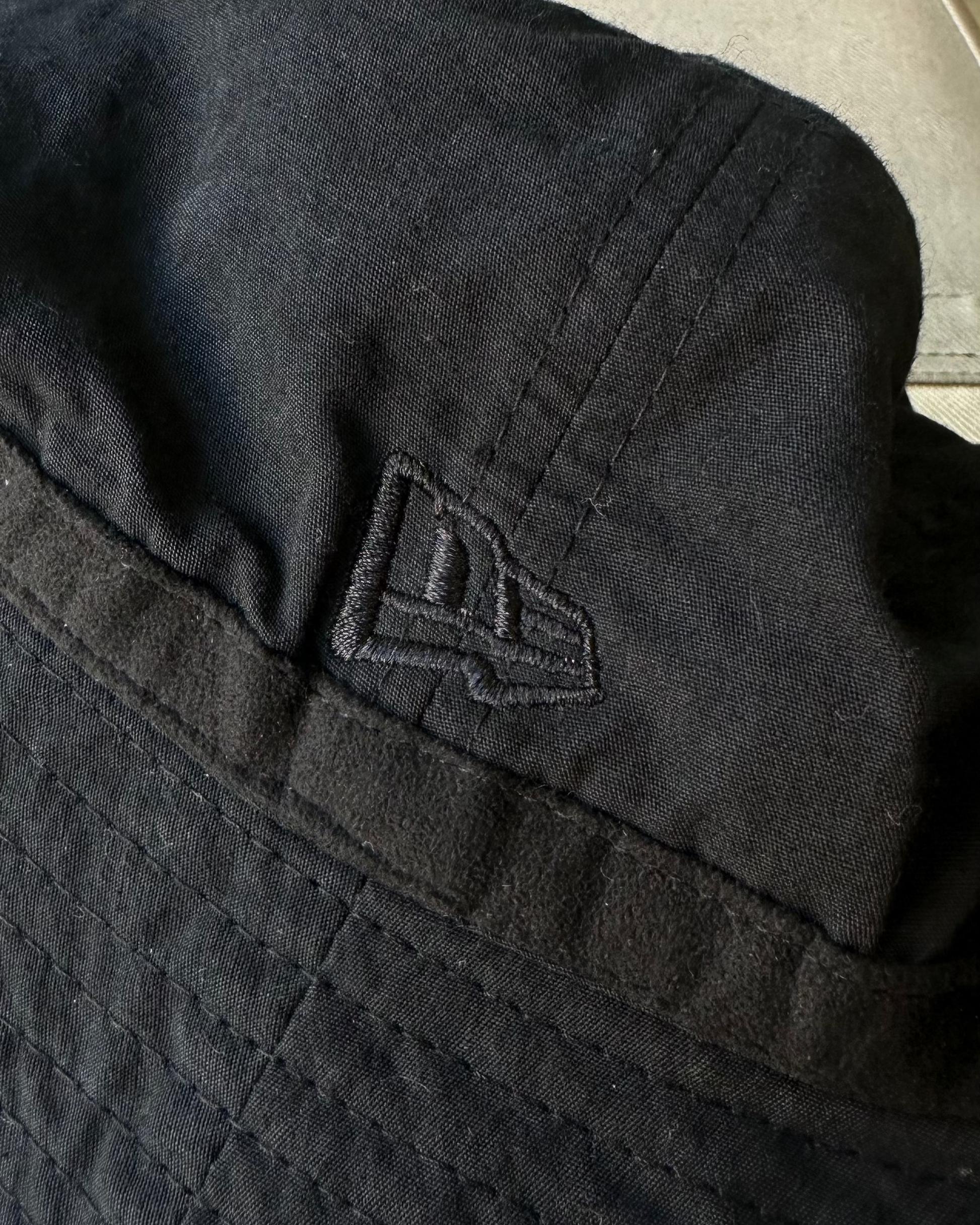 Black Song For The Mute x New Era bucket hat with a logo on a light-colored surface