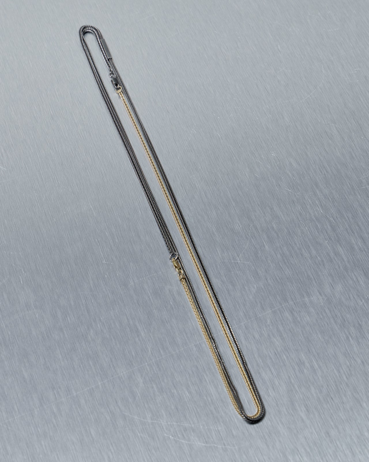 Long thin metal Stephanie Said necklace on a gray background