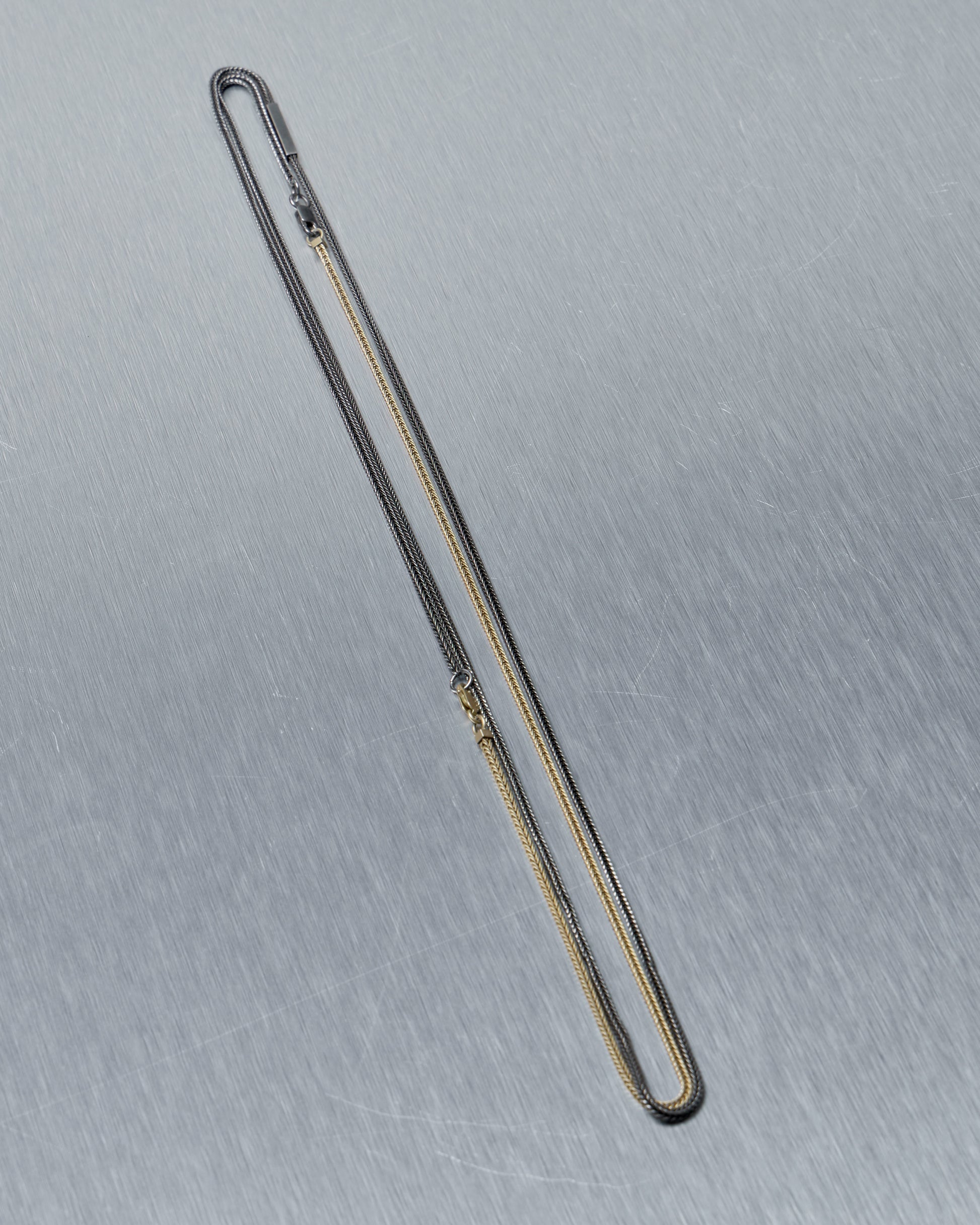 Long thin metal Stephanie Said necklace on a gray background