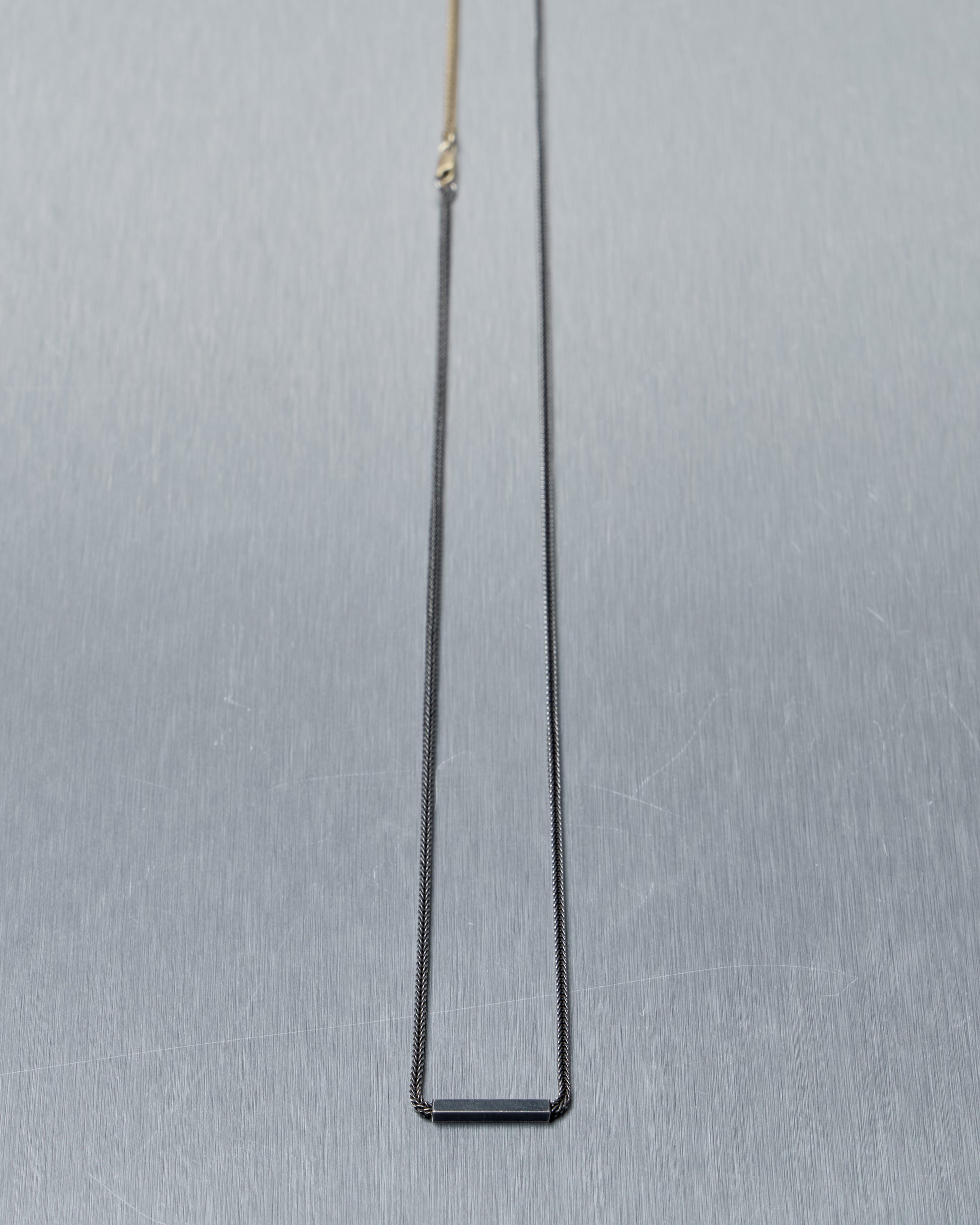 Thin black Stephanie Said rectangular pendant on a chain against a gray background