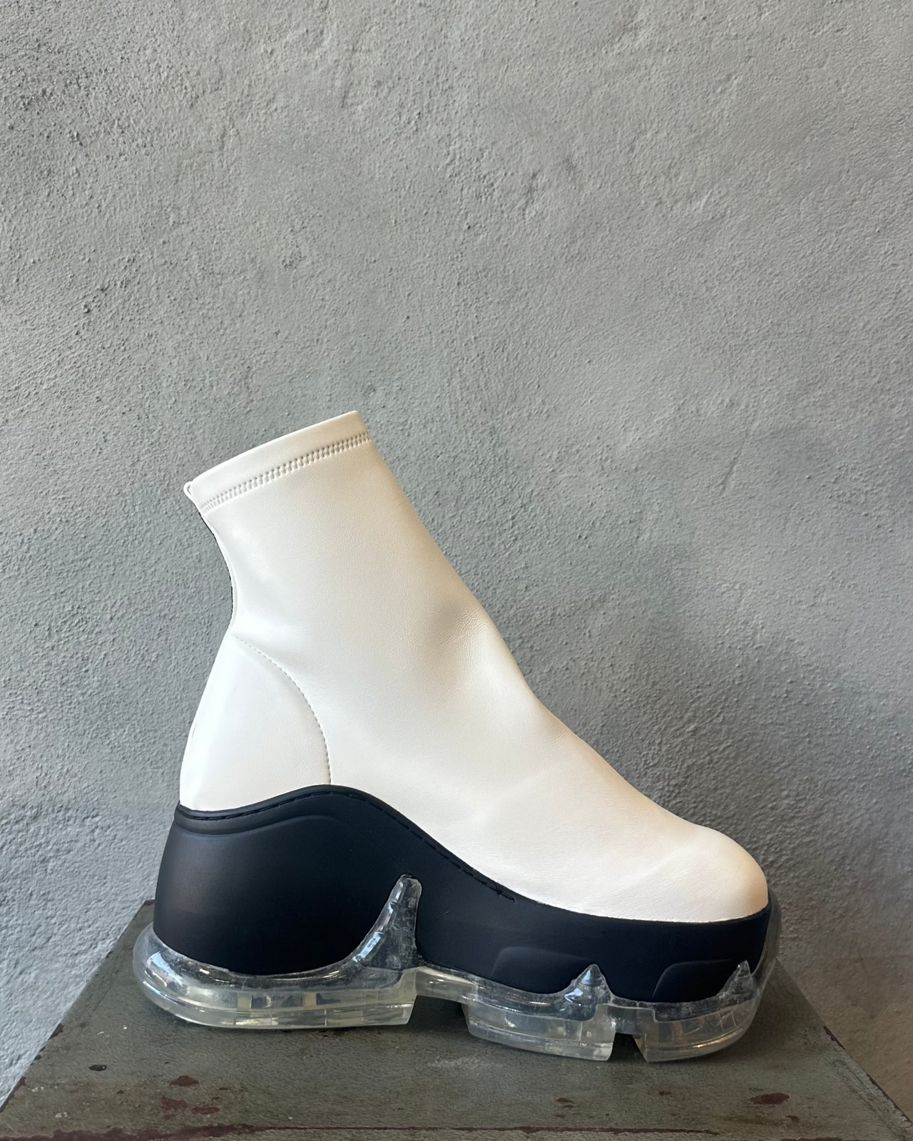 White and black high-top Swear London platform sneaker on a metal stool against a gray concrete wall.
