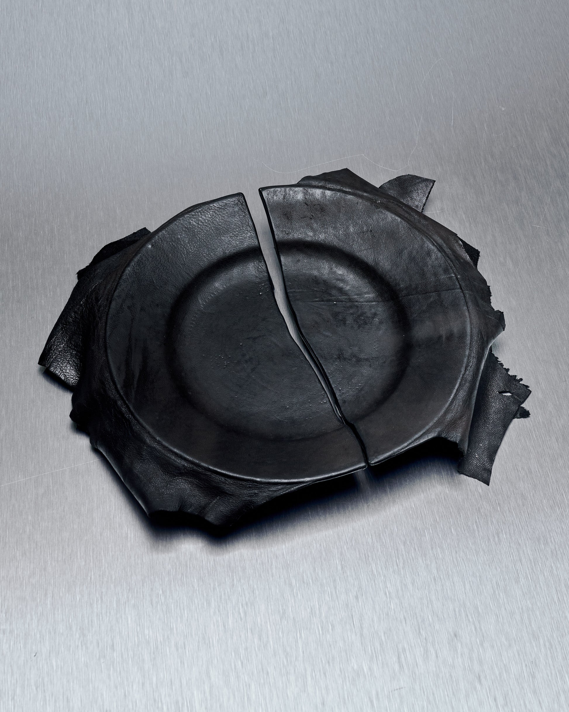 A photo of a ceramic plate from T.A.S Japan with a black lamb leather cover, showcasing the broken and repaired portions of the plate.