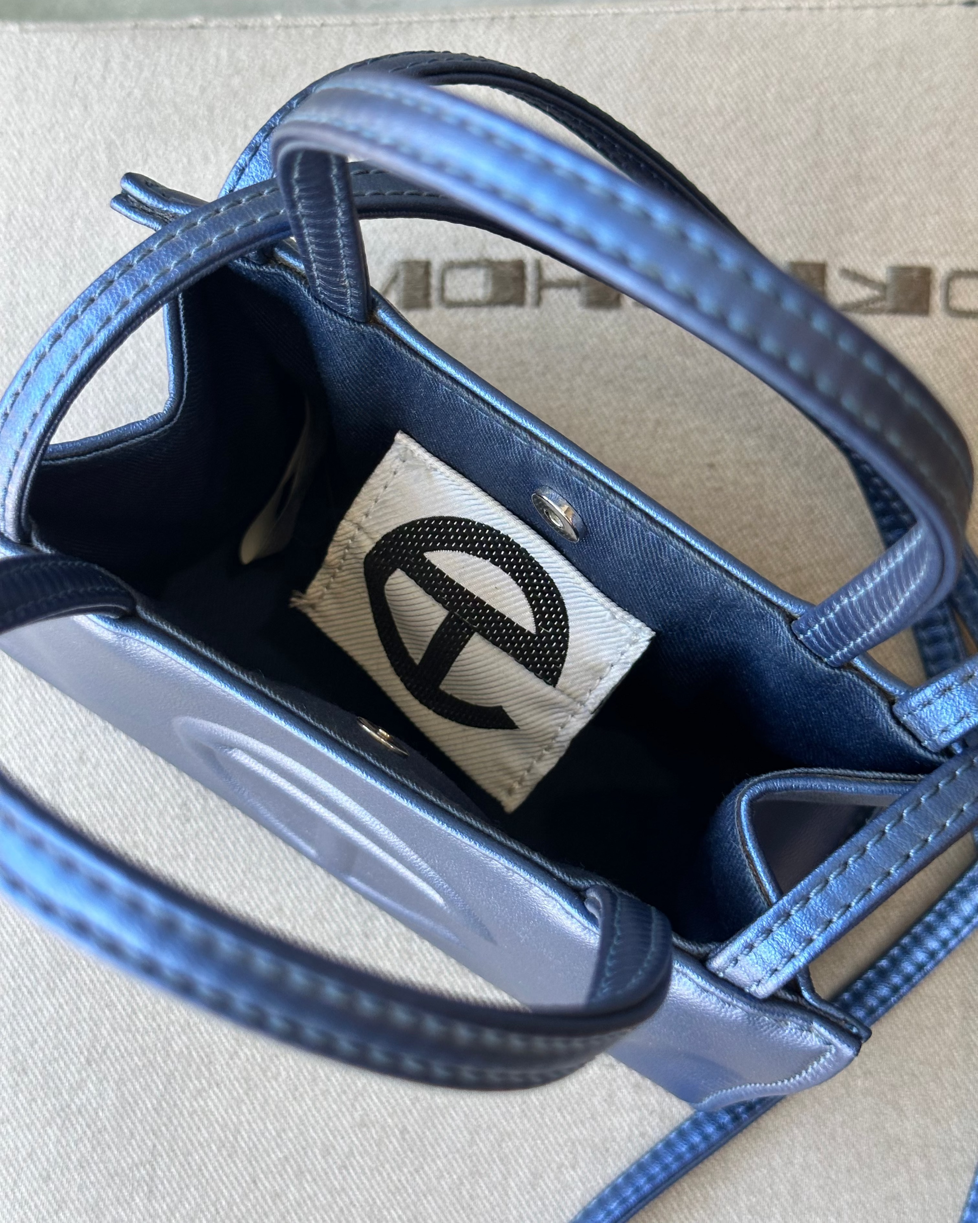 Close-up of a blue metallic Telfar mini bag with a brand label on a cardboard background