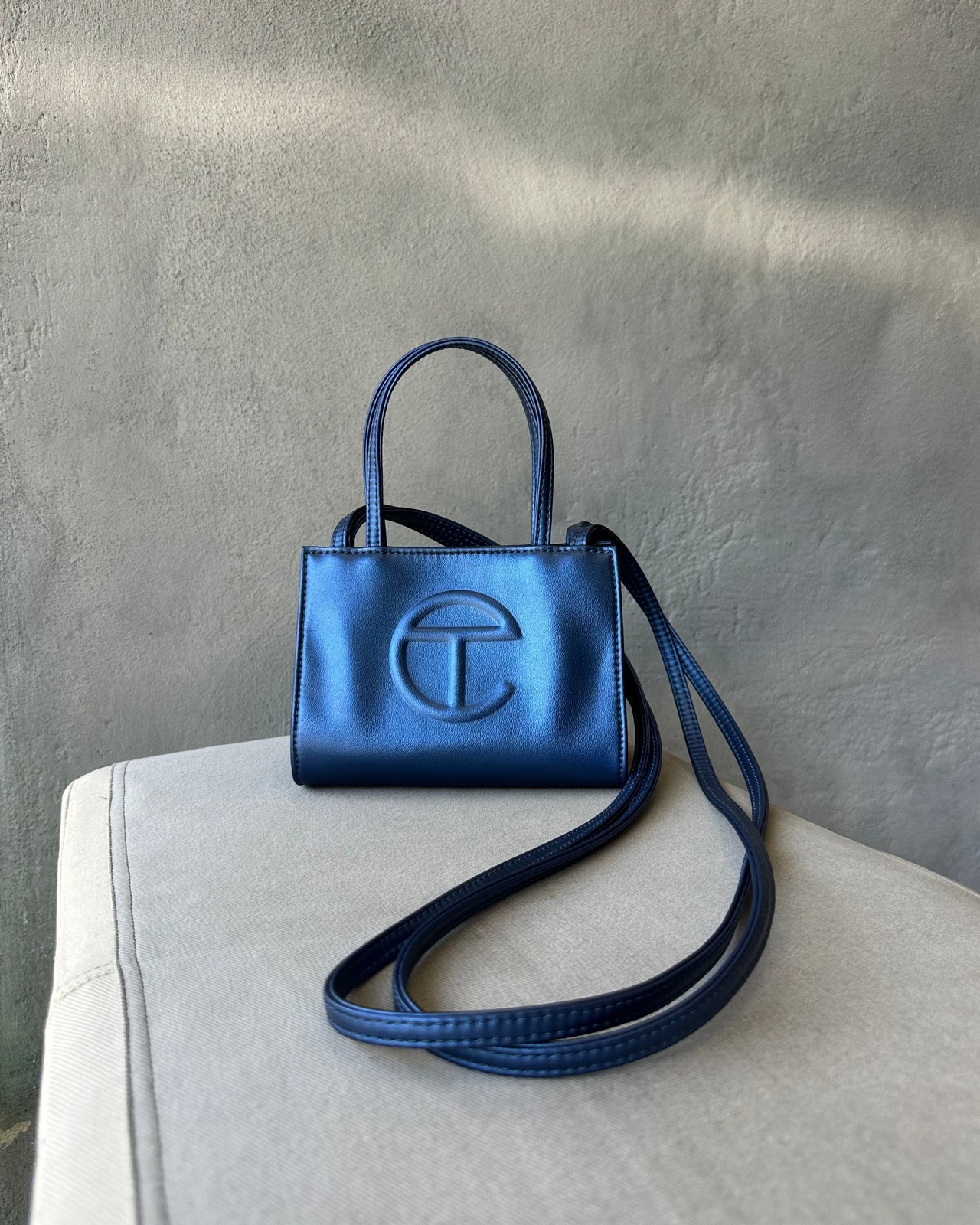 Blue Telfar handbag with a strap on a light gray surface against a textured gray wall.