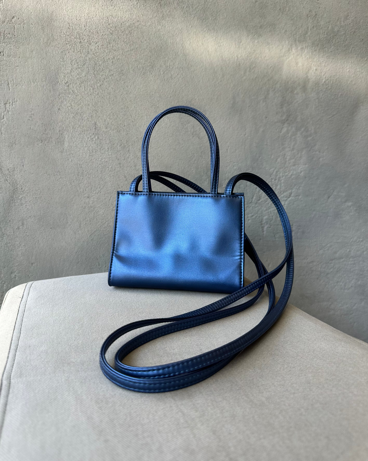 Blue Telfar handbag with a strap on a light gray surface against a textured gray wall.