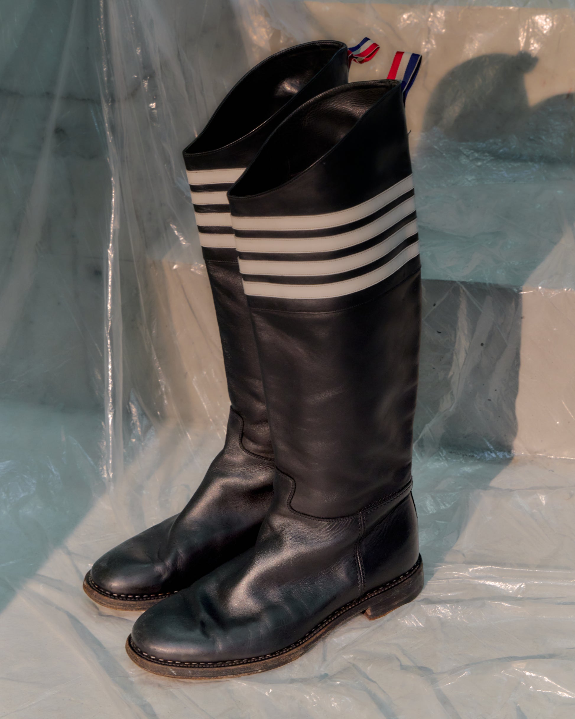 Black knee-high Thom Browne boots with striped socks on a transparent background