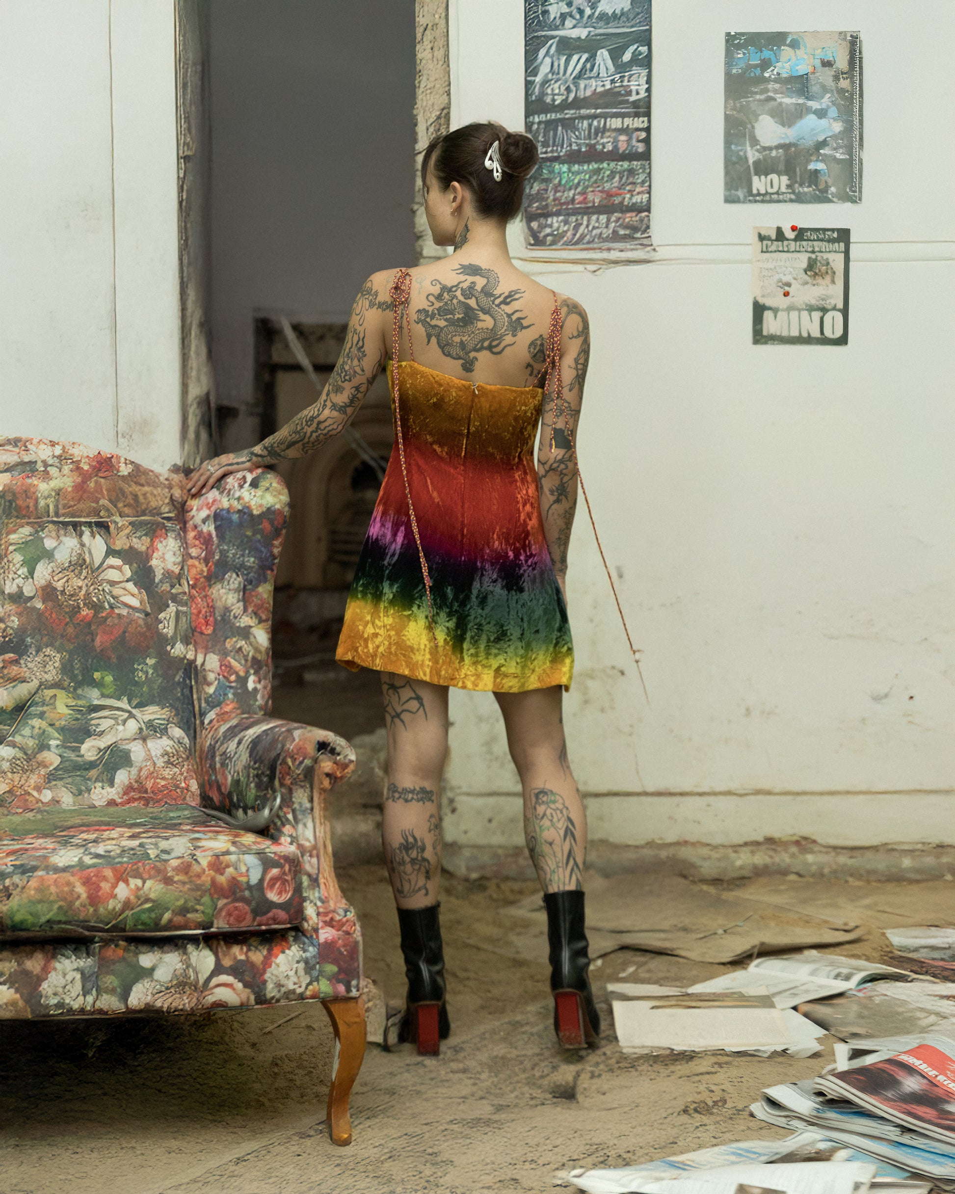 Person wearing a colourful Todd Oldham dress in an abandoned room with posters on the wall.