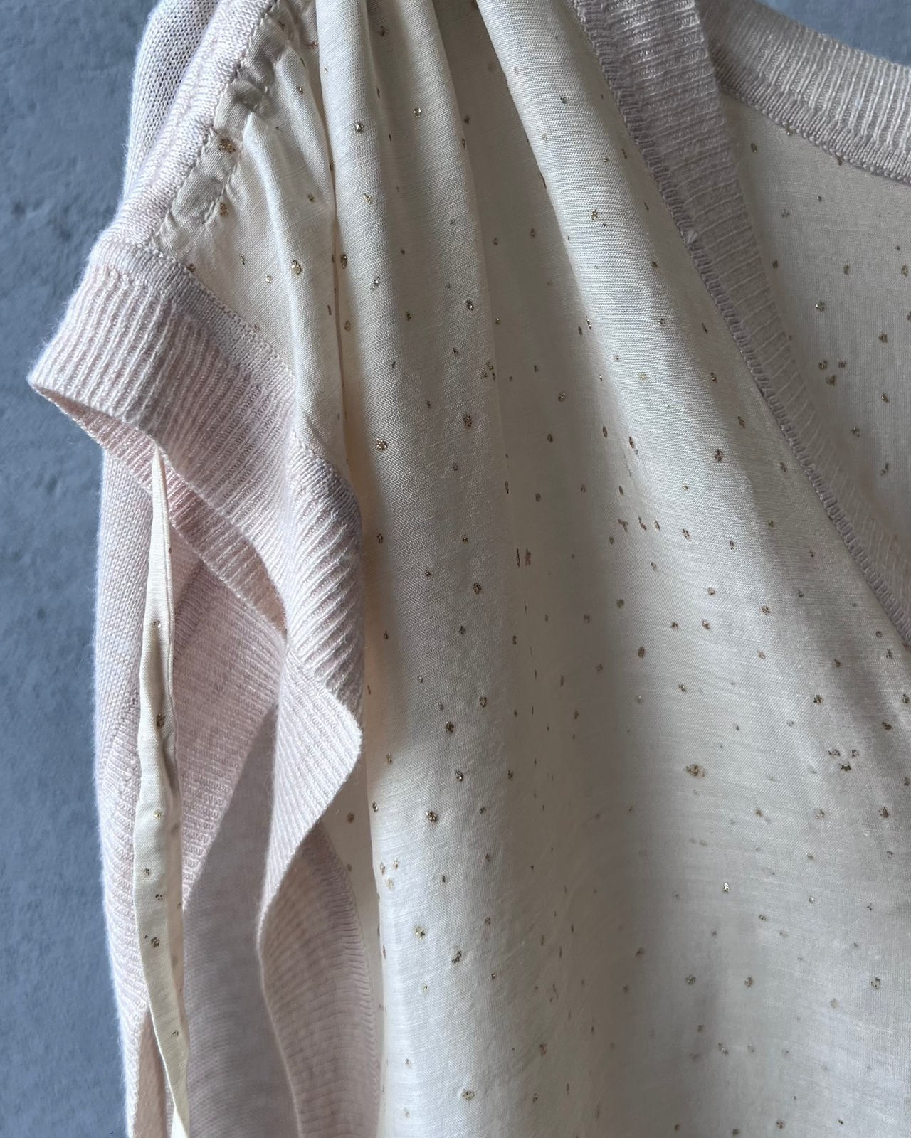 Beige sleeveless Tsumori Chisato top hanging on a rack against a gray wall