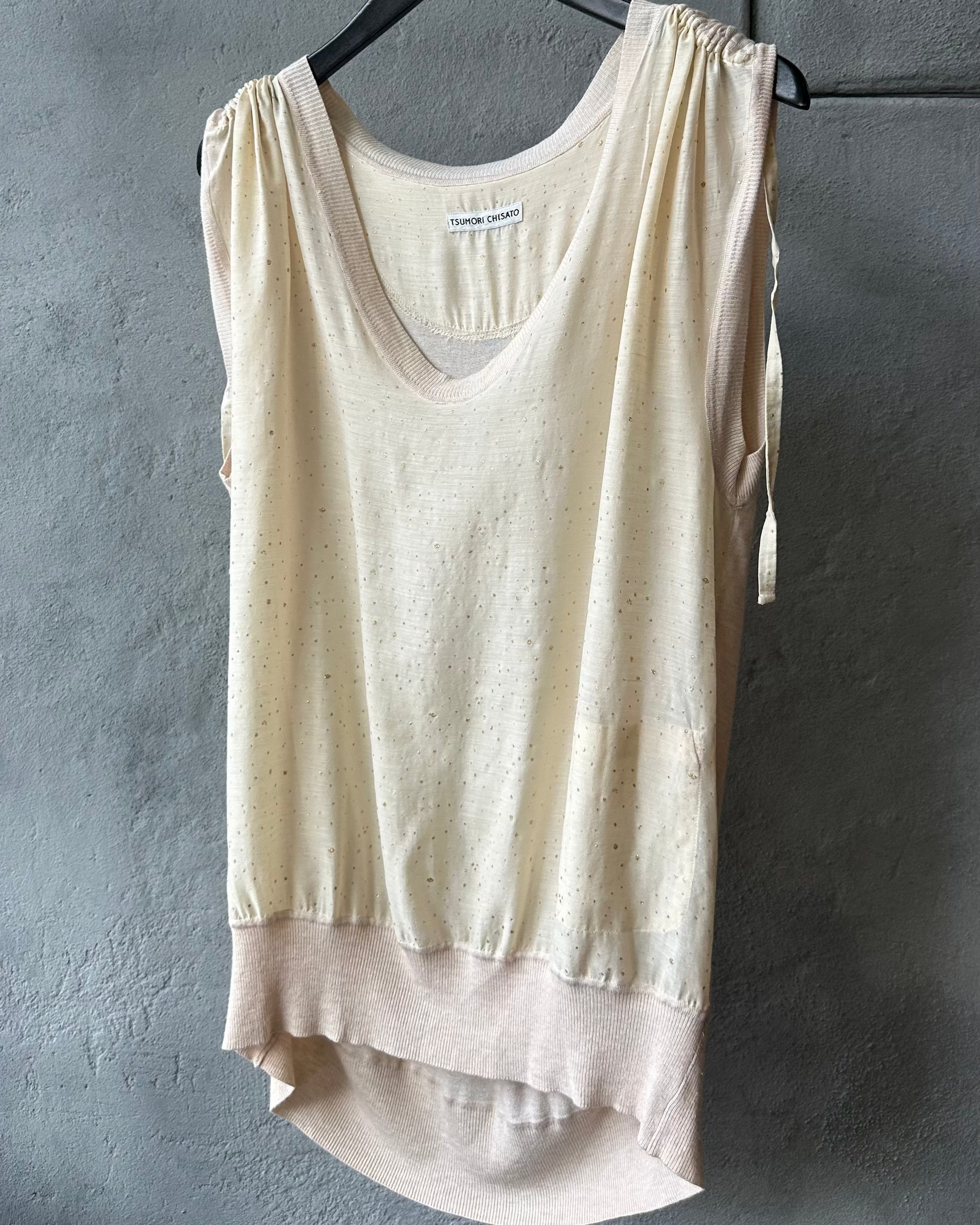 Beige sleeveless Tsumori Chisato top hanging on a rack against a gray wall
