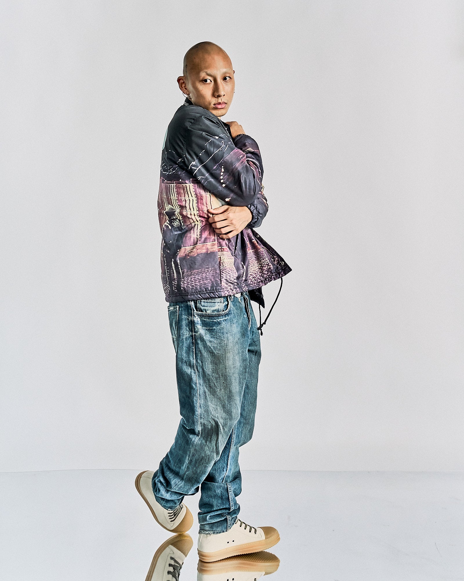 A person wearing a long-sleeved, plaid-patterned, button-up Undercover coach jacket with a visible '2001: A Space Odyssey' movie poster-inspired graphic on the front. The jacket has a faux fur lining and is paired with blue jeans and sneakers.