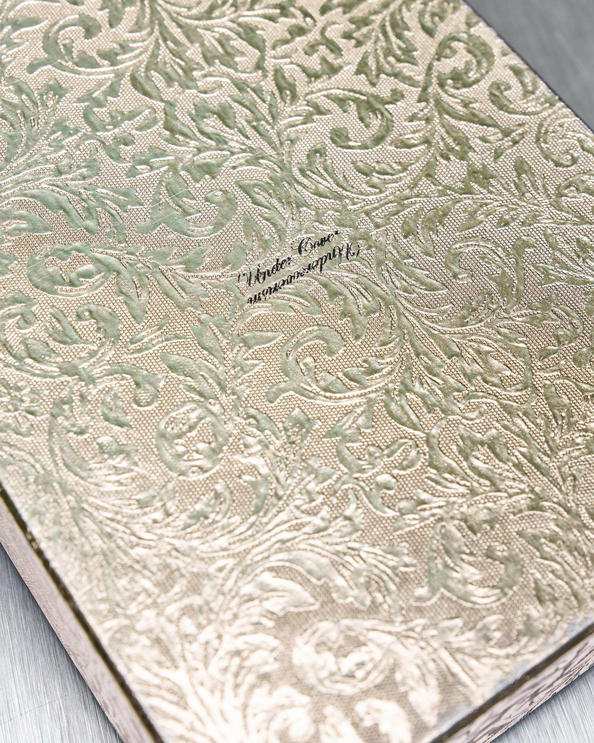 Elegant gift box cover with embossed floral pattern in green and gold. Centred text reads "Under Cover."