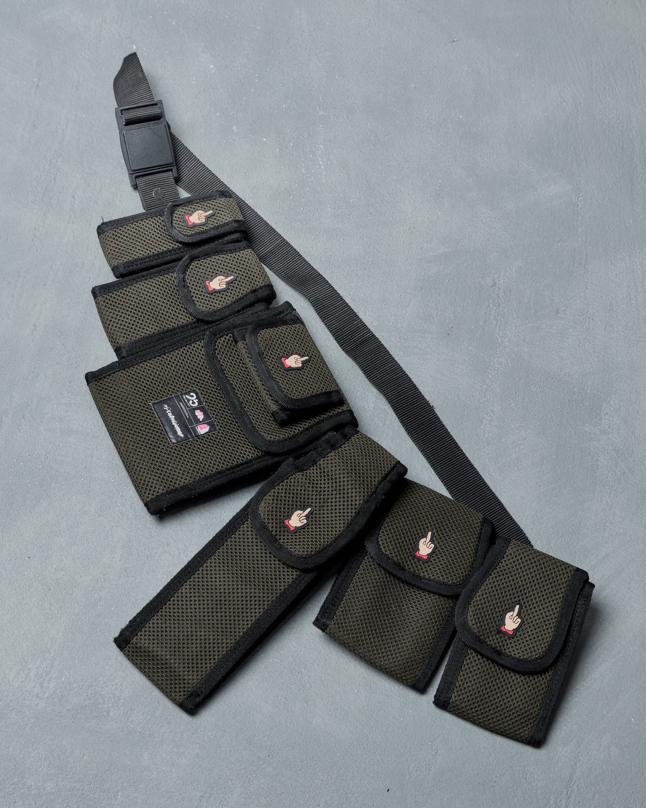 Black tactical belt bag by Undercover with multiple pouches on a gray background