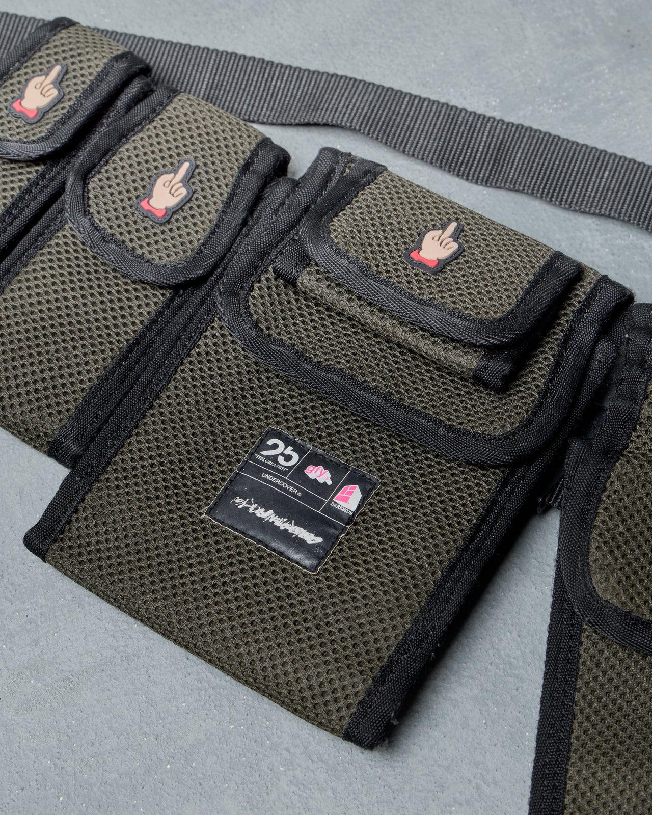 Black tactical belt bag by Undercover with multiple pouches on a gray background