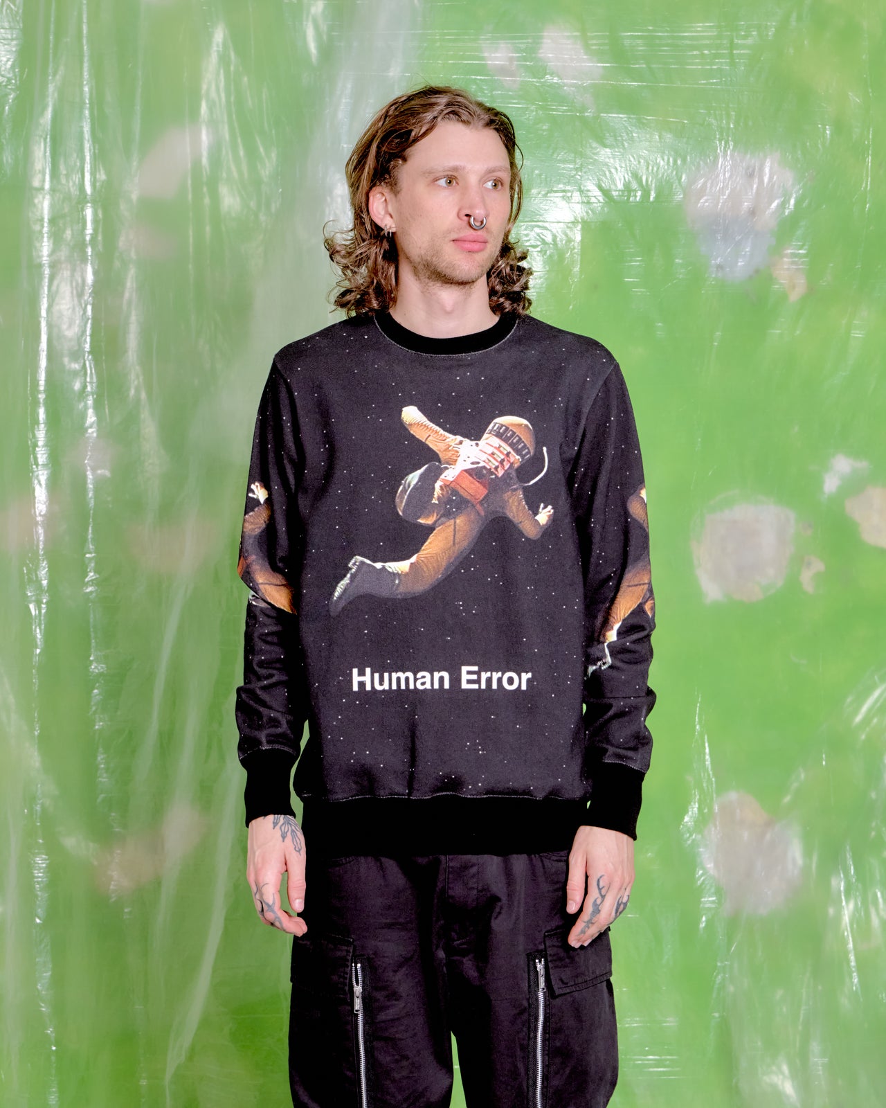 Person wearing a black Undercover x Stanley Kubrick sweatshirt with a graphic design and text, standing against a green background.