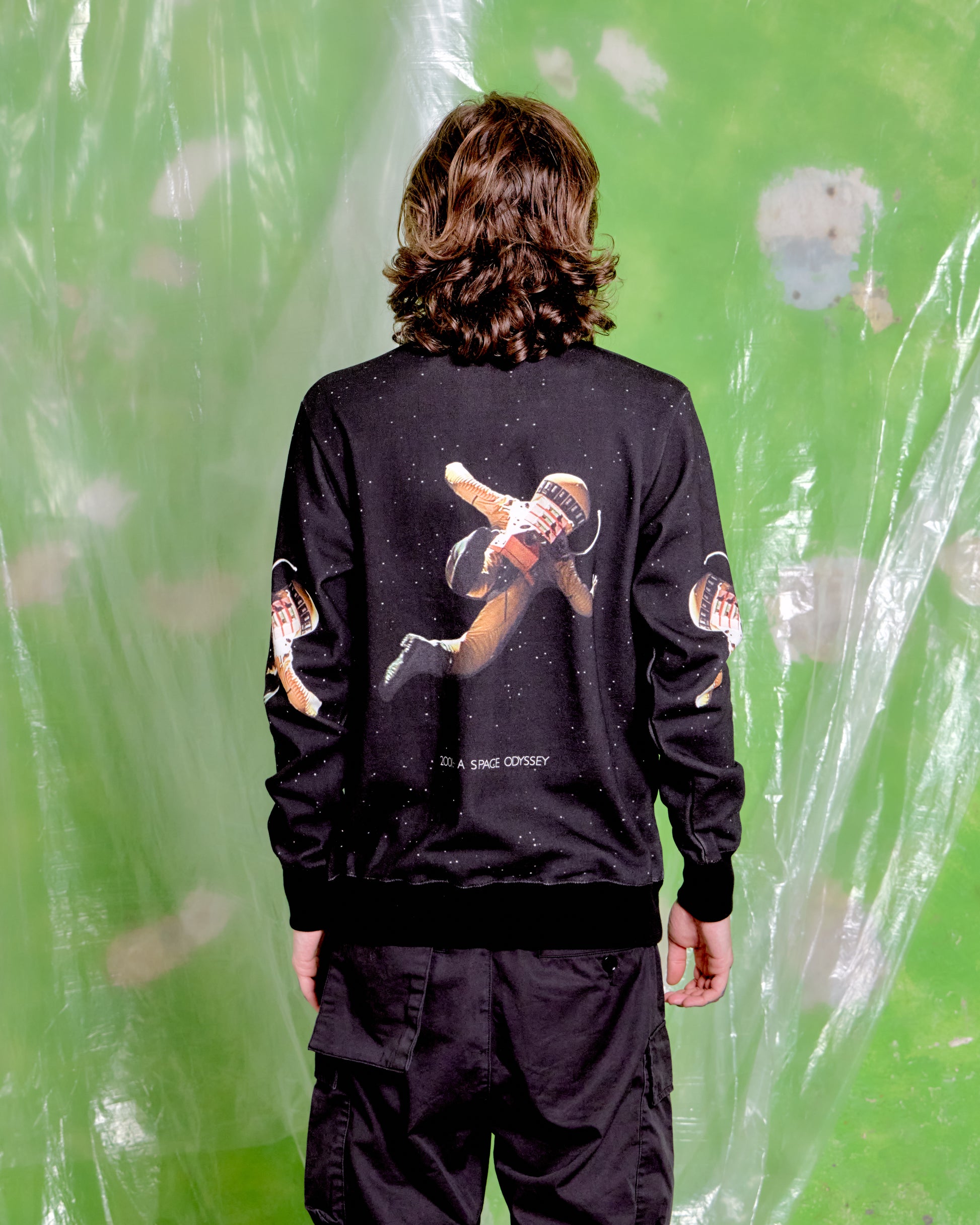 Person wearing a black Undercover x Stanley Kubrick jacket with a graphic design on the back against a green background