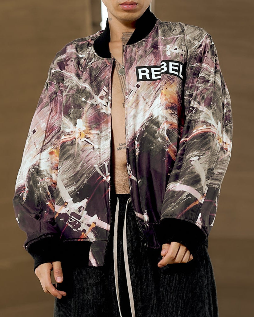 A person wearing a reversible Undercover x Star Wars bomber jacket with multicolour graphics, featuring text and geometric patterns on the sleeves, standing in a tunnel-like setting.