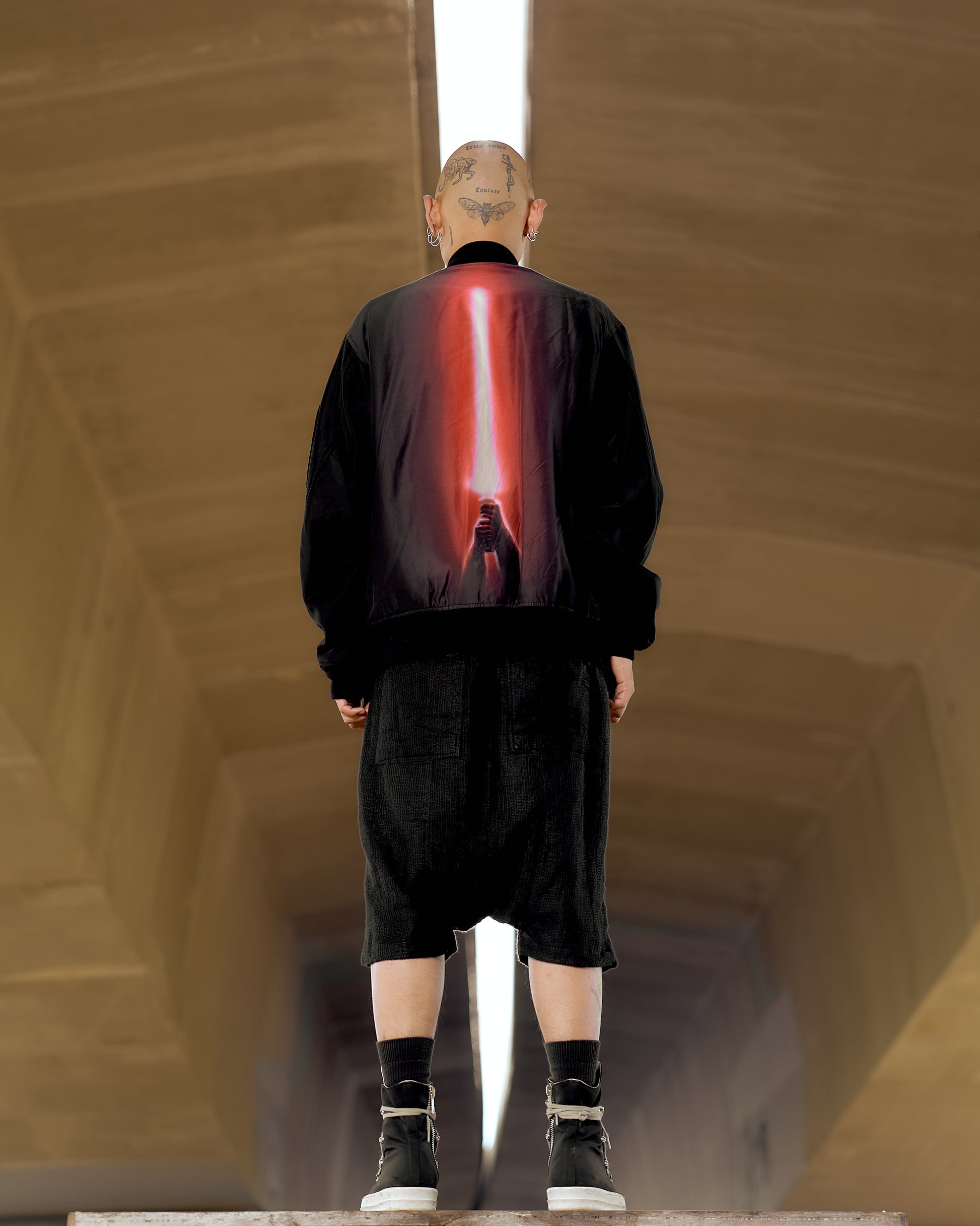 A person viewed from behind wearing a reversible Undercover x Star Wars bomber jacket with a red graphic on the back, standing in a tunnel-like setting.