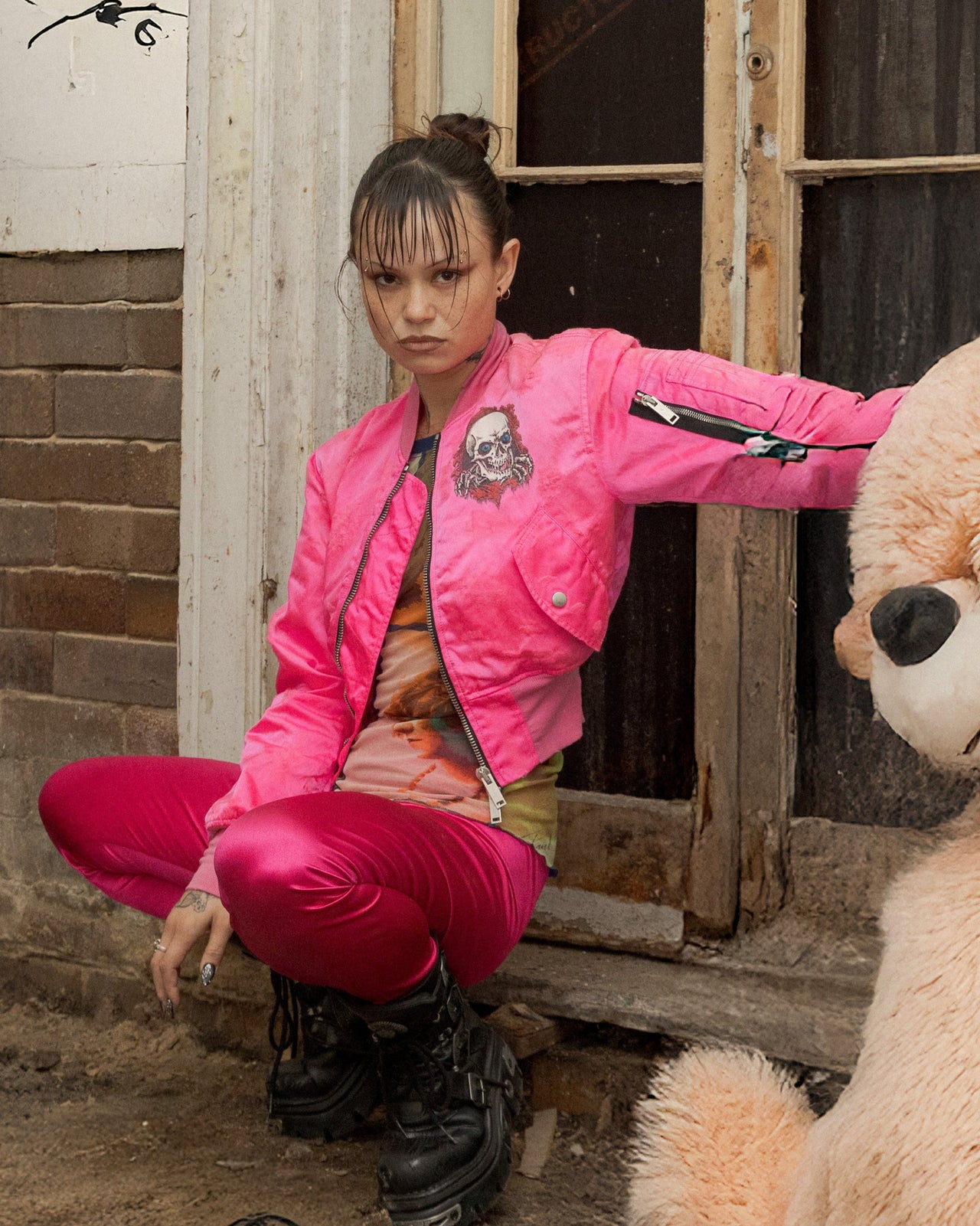 Person in a pink Unravel Project jacket interacting with a large teddy bear in a dilapidated room.