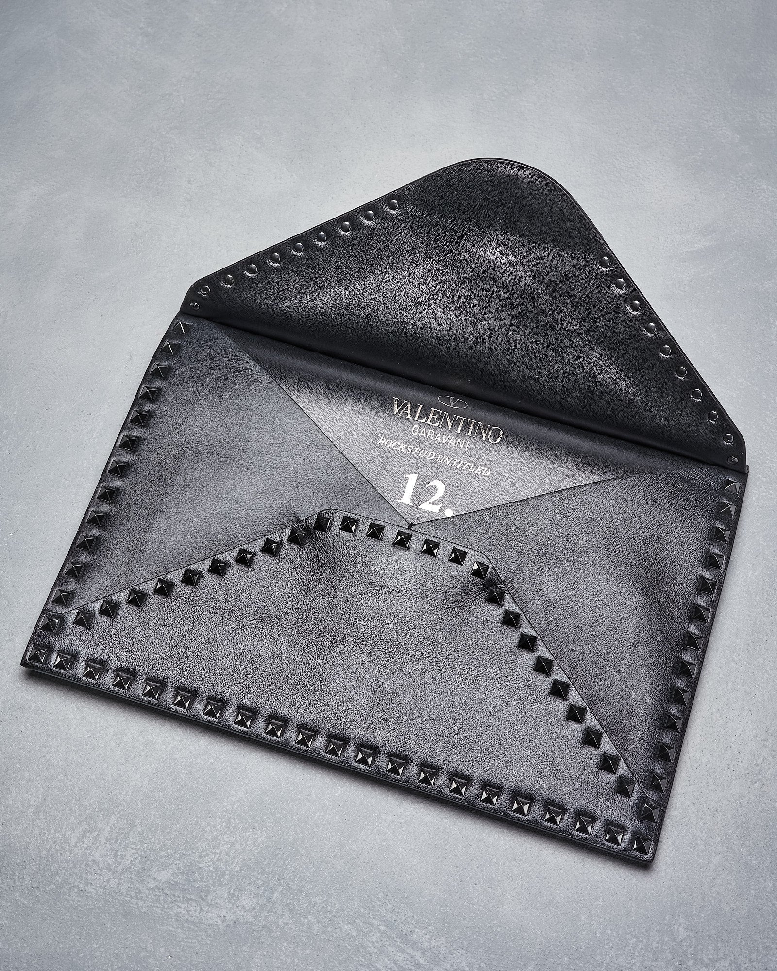 A sophisticated black leather Valentino envelope clutch, embellished with studded detailing. The interior reveals the brand name, exuding elegance and luxury.