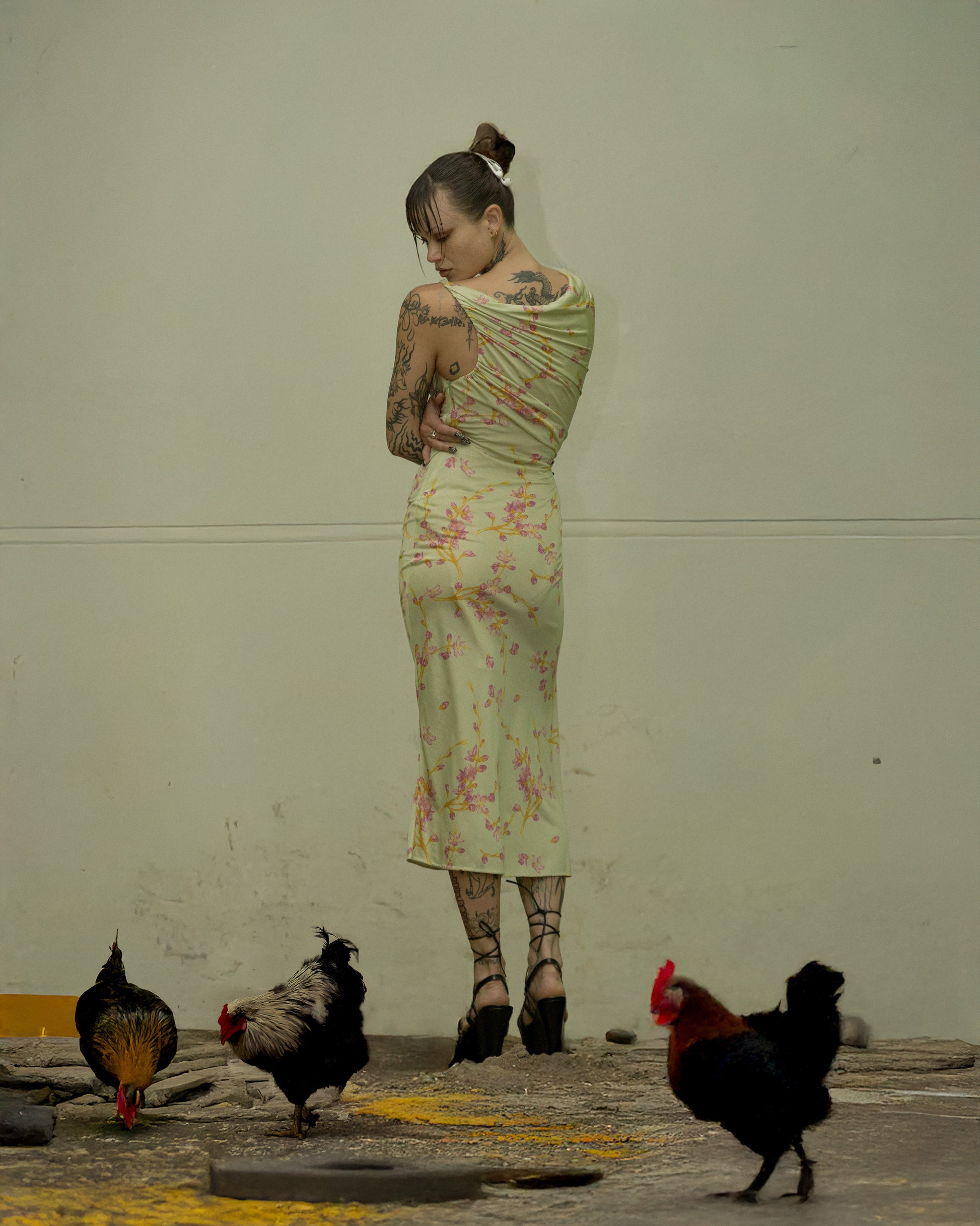 Woman in a floral Versace dress standing with chickens around her on a concrete floor.