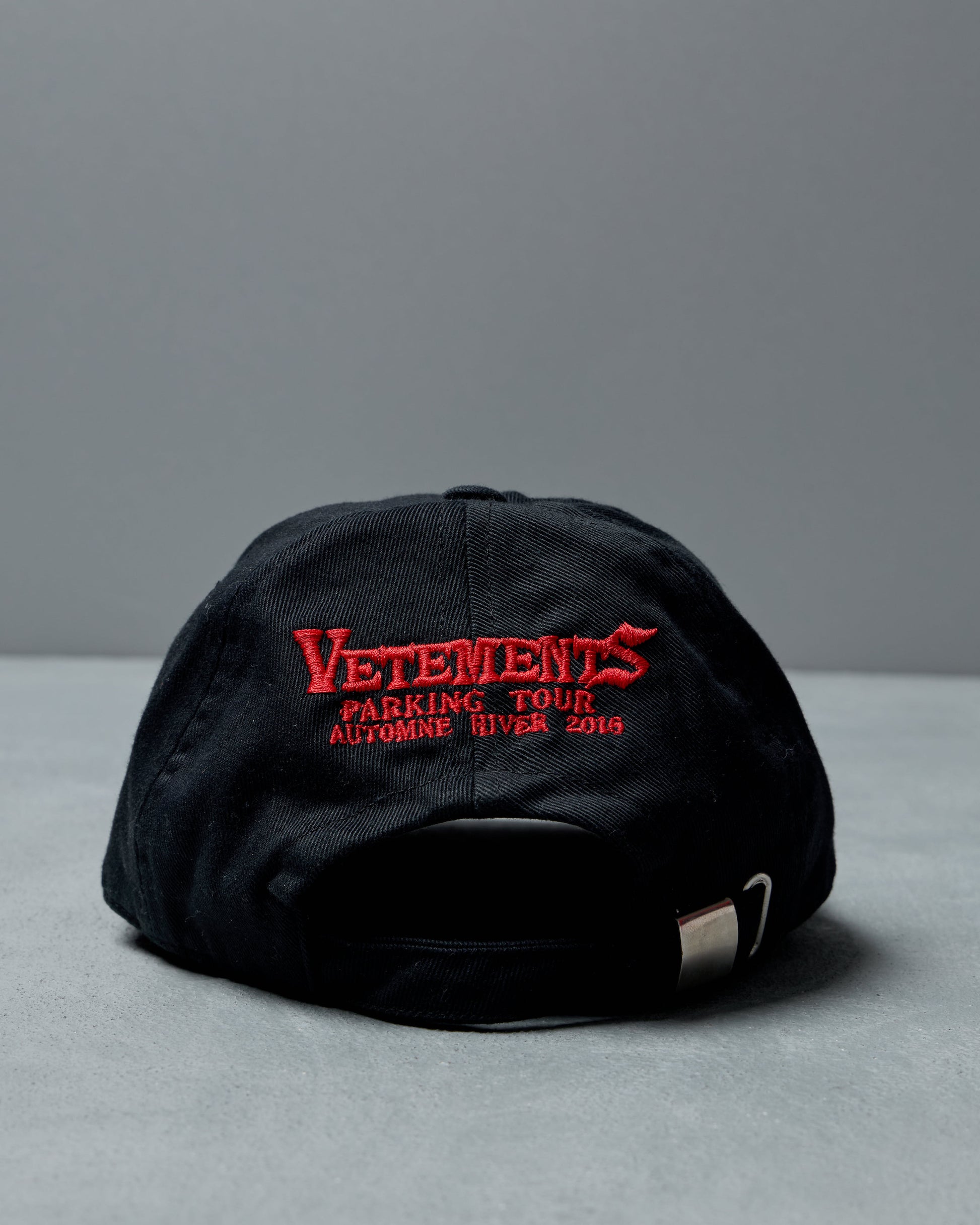 Black Vetements cap with red embroidered text on a gray background