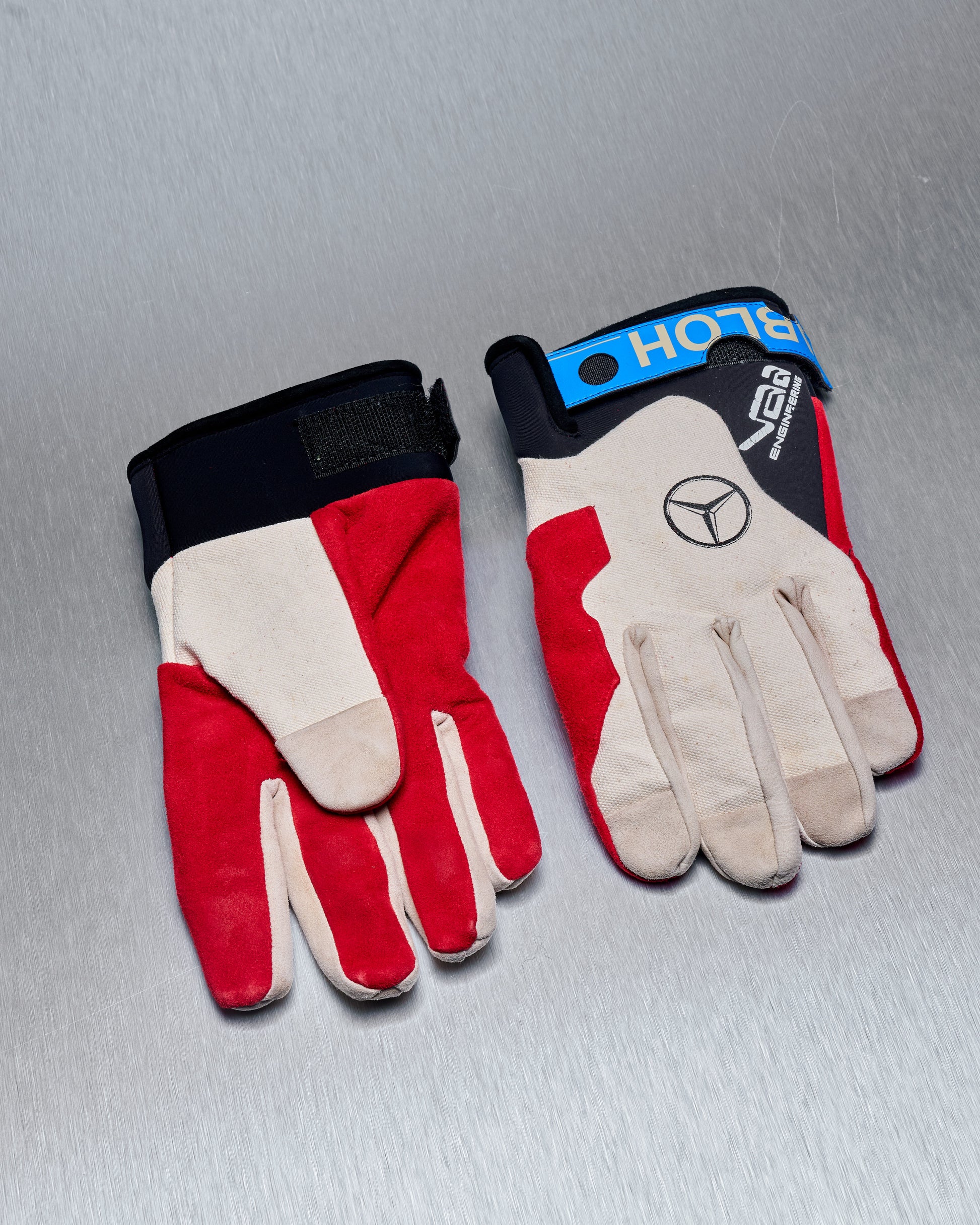 Pair of red and beige Virgil Abloh x Mercedes Benz gloves on a grey surface. One glove displays a Mercedes logo.