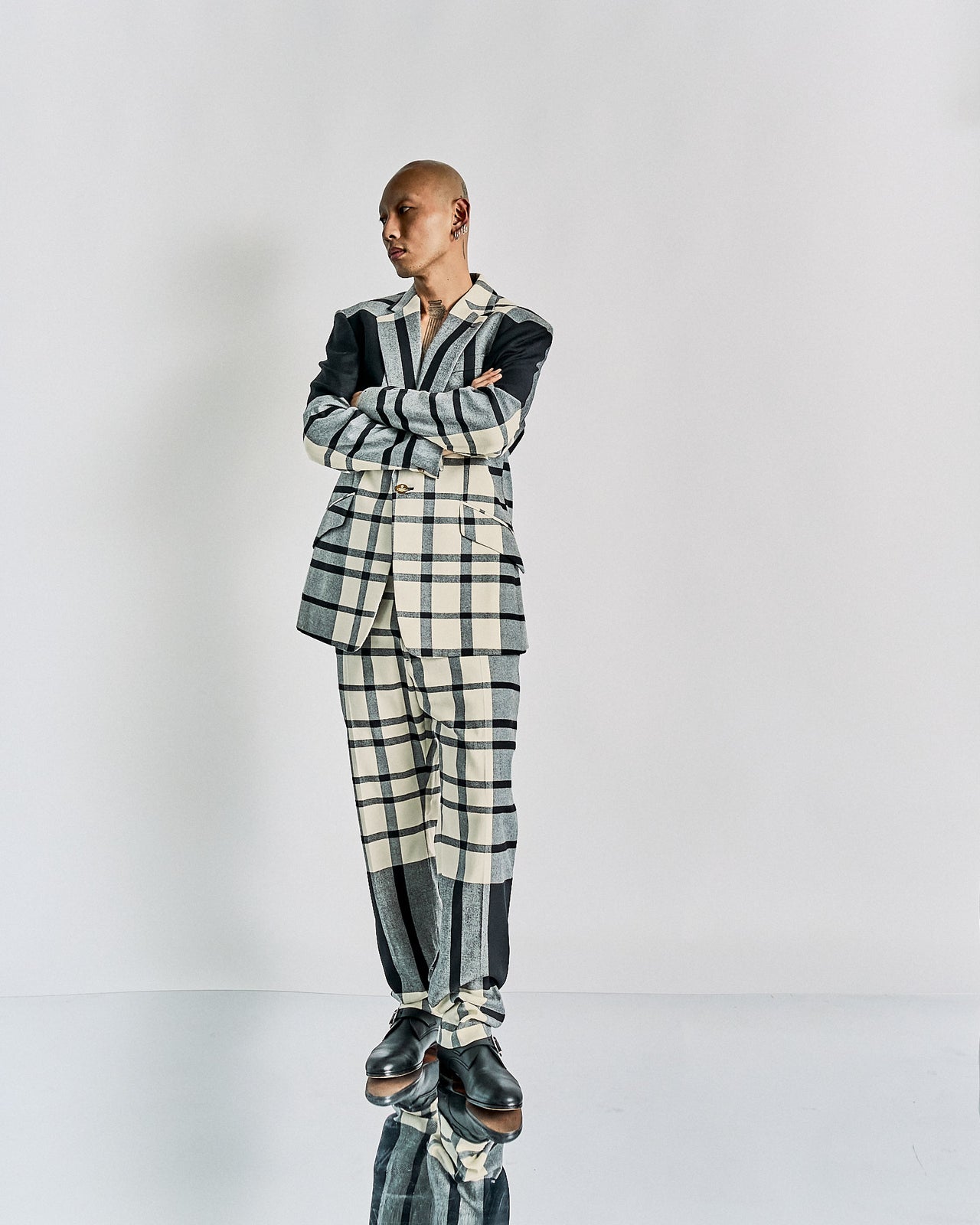 A person stands against a plain backdrop, wearing a checkered Vivienne Westwood suit with varying patterns in black and cream tones. The expression is neutral and relaxed.