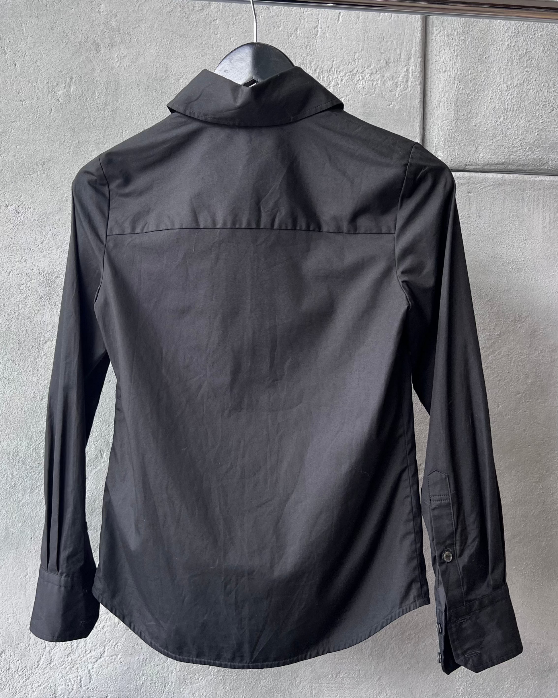 Black Vivienne Westwood shirt on a hanger against a gray wall