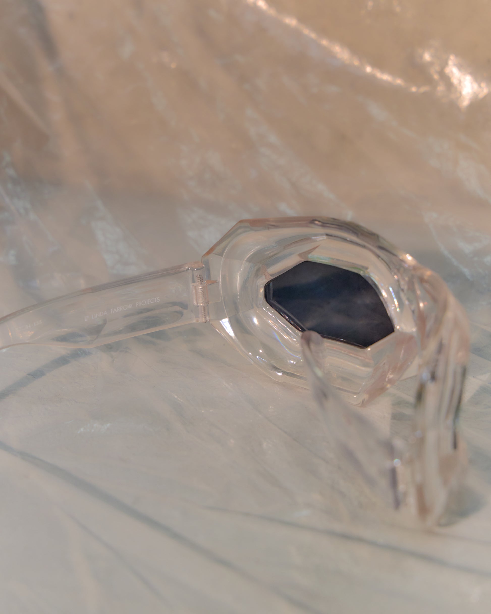 Clear plastic Walter Van Beirendonck x Linda Farrow sunglasses on a reflective surface