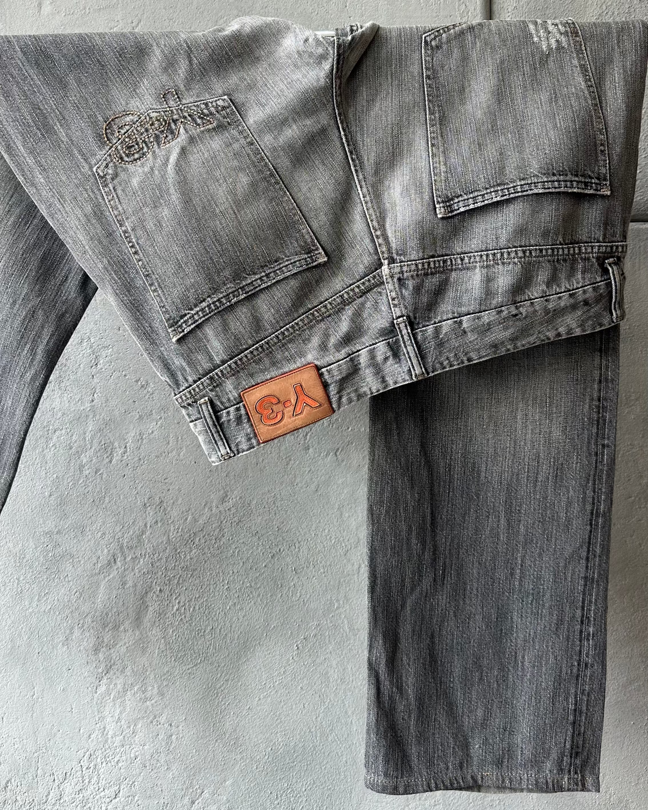 Gray Y-3 jeans with a brand logo on a textured gray background
