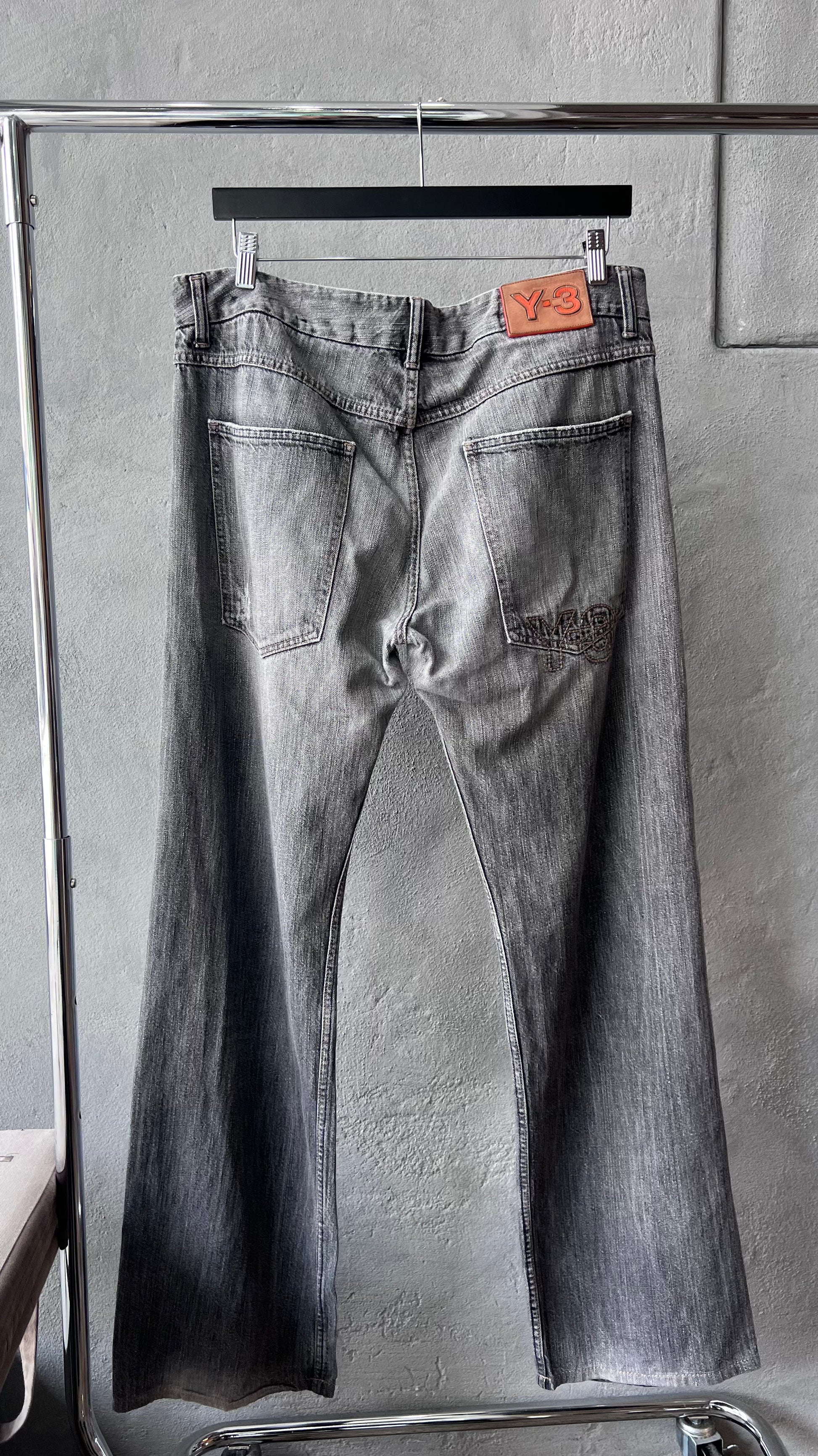 Pair of gray Y-3 jeans hanging on a rack against a neutral background